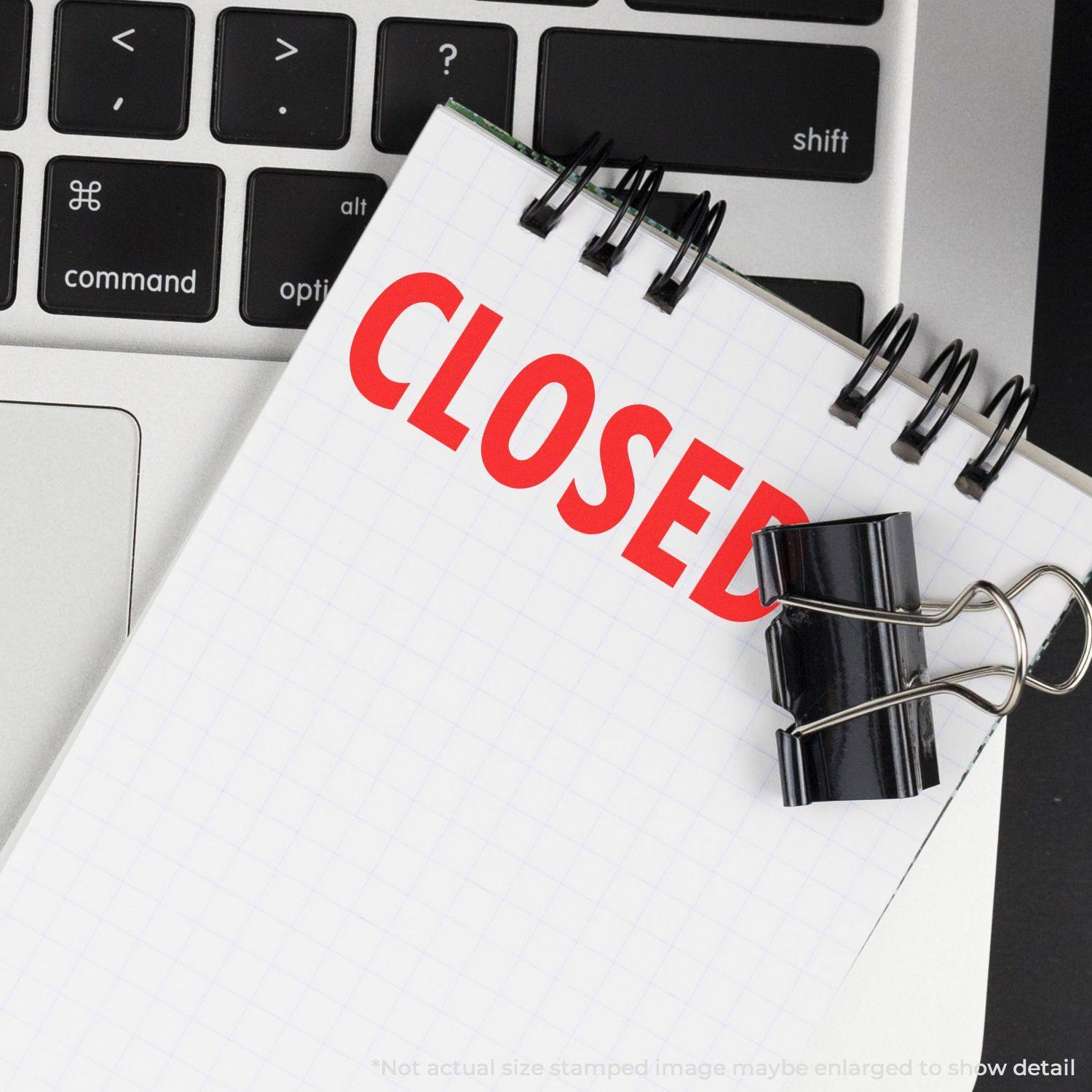 Large Self Inking Closed Stamp marking CLOSED in red on a notepad, placed on a laptop keyboard with a black binder clip.