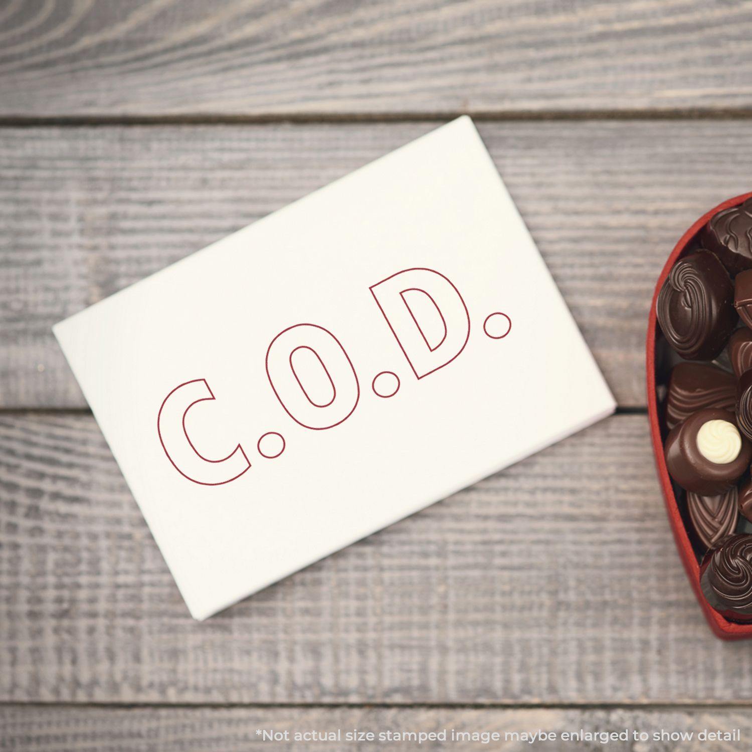 COD With Outline Text Rubber Stamp used on a white card placed on a wooden surface next to a heart-shaped box of chocolates.