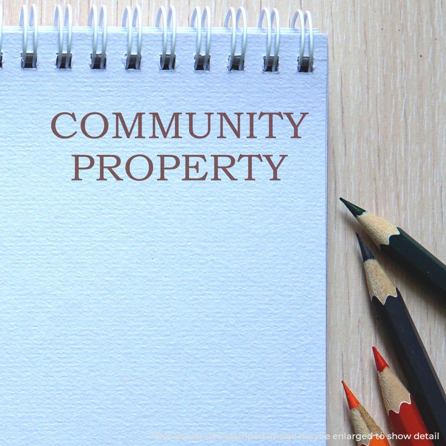 Large Self Inking Community Property Stamp used on a spiral notebook, with colored pencils nearby on a wooden surface.