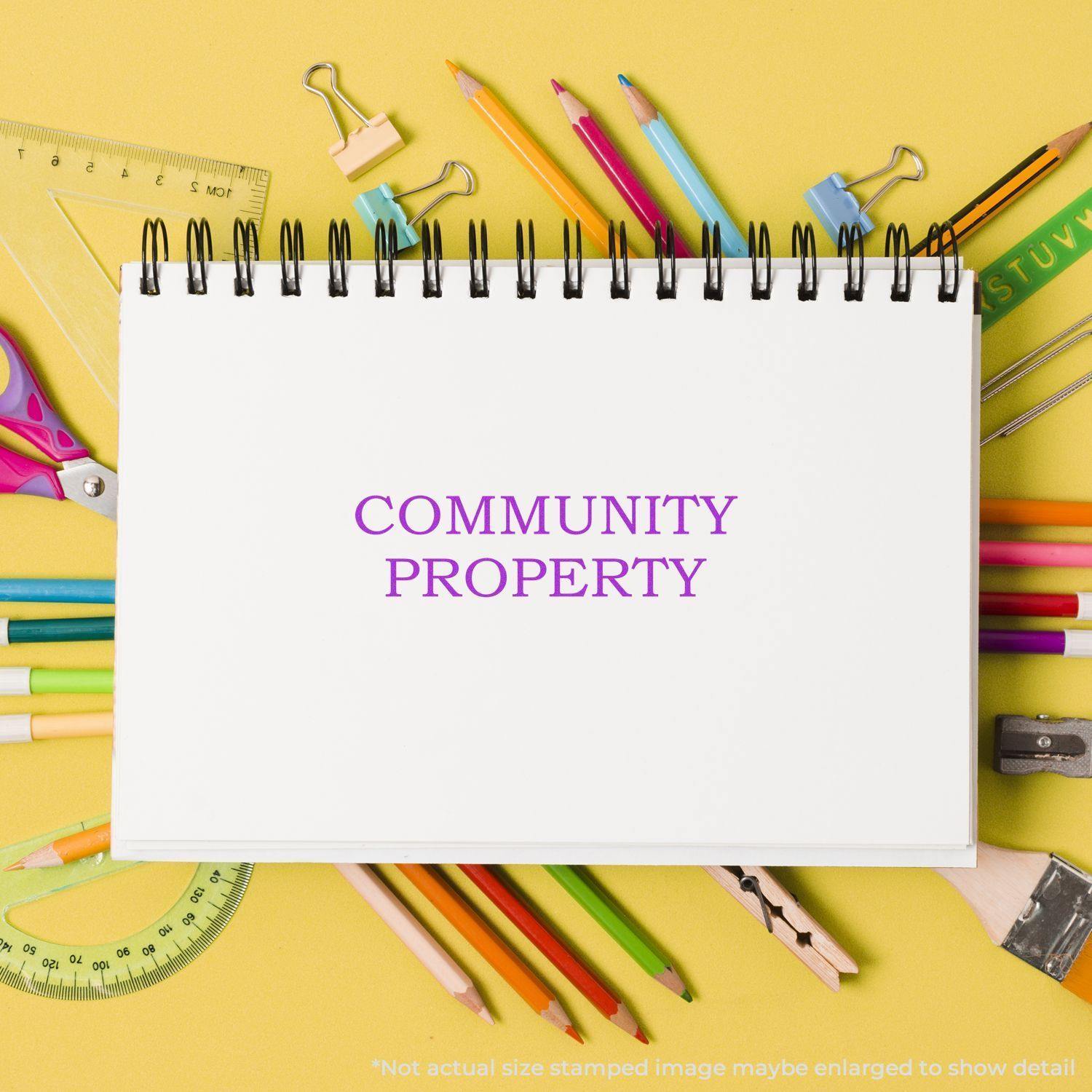 Large Self Inking Community Property Stamp used on a white notebook surrounded by colorful stationery on a yellow background.