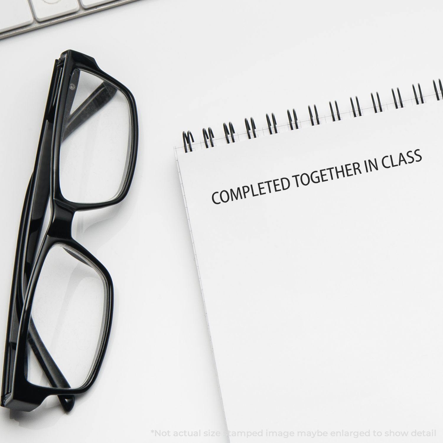 Glasses next to a spiral notebook with the text COMPLETED TOGETHER IN CLASS stamped on the page using the Large Self Inking Completed Together Stamp.