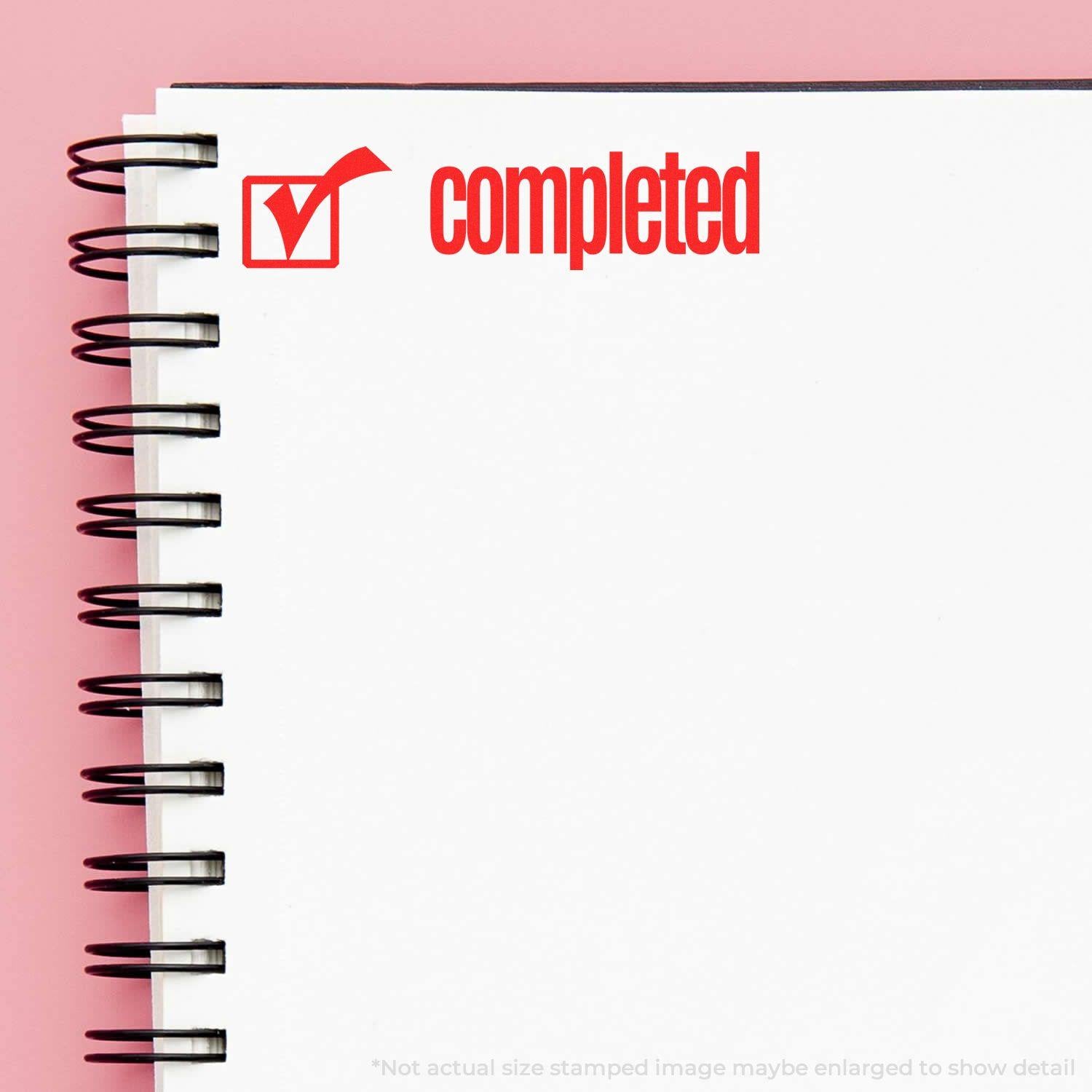 Slim Pre-Inked Completed with Checkbox Stamp in red ink on a white spiral notebook page against a pink background.