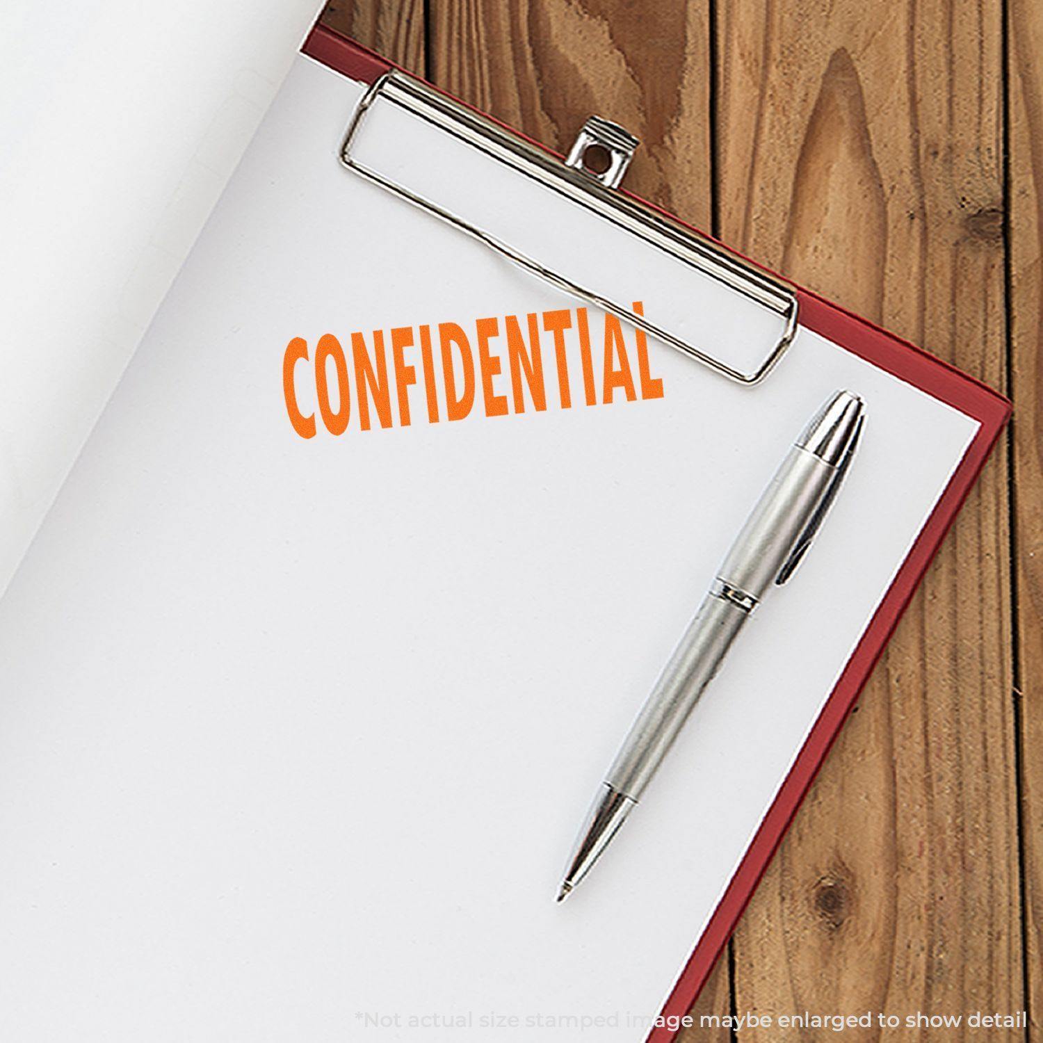 A clipboard with a sheet of paper stamped CONFIDENTIAL in red ink using the Large Self Inking Confidential Stamp, placed next to a silver pen on a wooden surface.