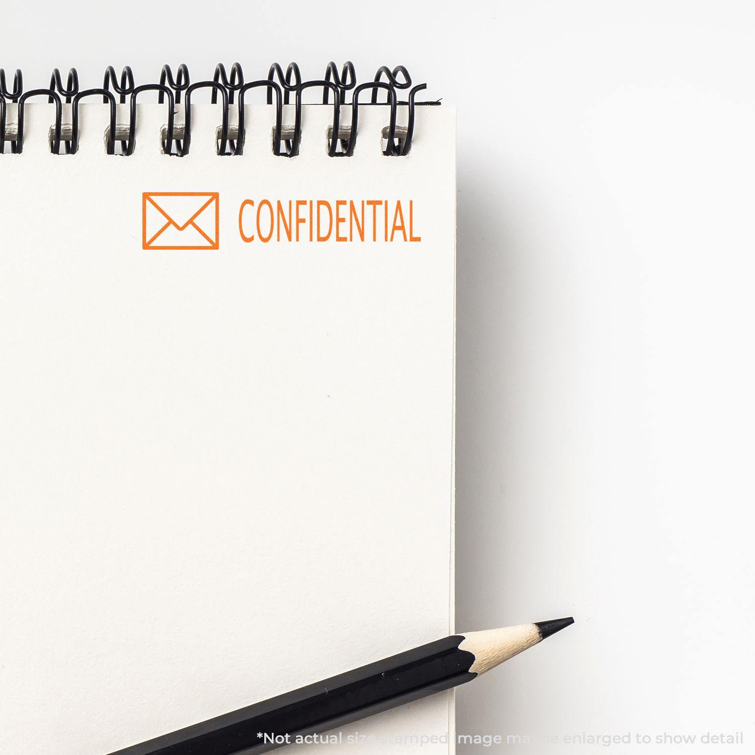 Slim Pre-Inked Confidential with Envelope Stamp on a spiral notebook, next to a pencil, highlighting the word CONFIDENTIAL.