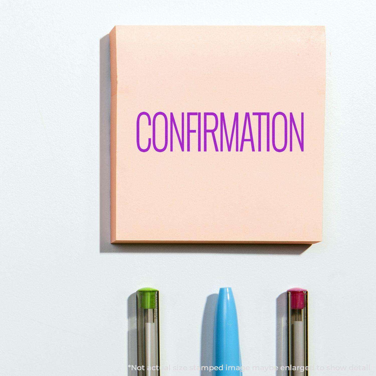 Confirmation Rubber Stamp used on a pink sticky note, with three pens below it on a white surface.