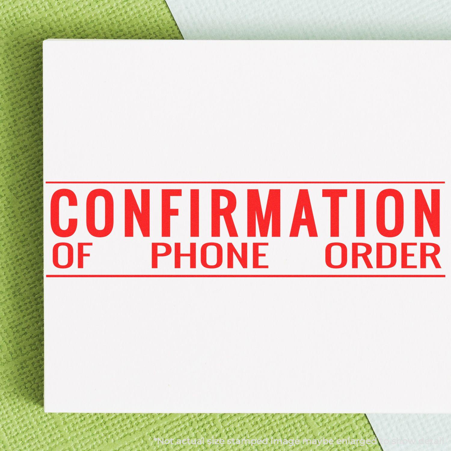 Red Slim Pre-Inked Confirmation of Phone Order Stamp on white paper, placed on a green and white textured background.