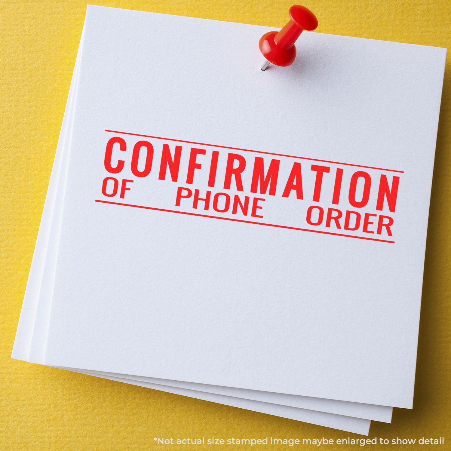 A stack of white papers with a red Confirmation of Phone Order Rubber Stamp imprint, pinned with a red pushpin on a yellow surface.