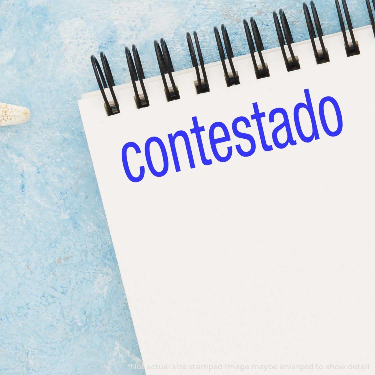 Slim Pre-Inked Contestado Stamp imprint on a white notepad with a blue background.