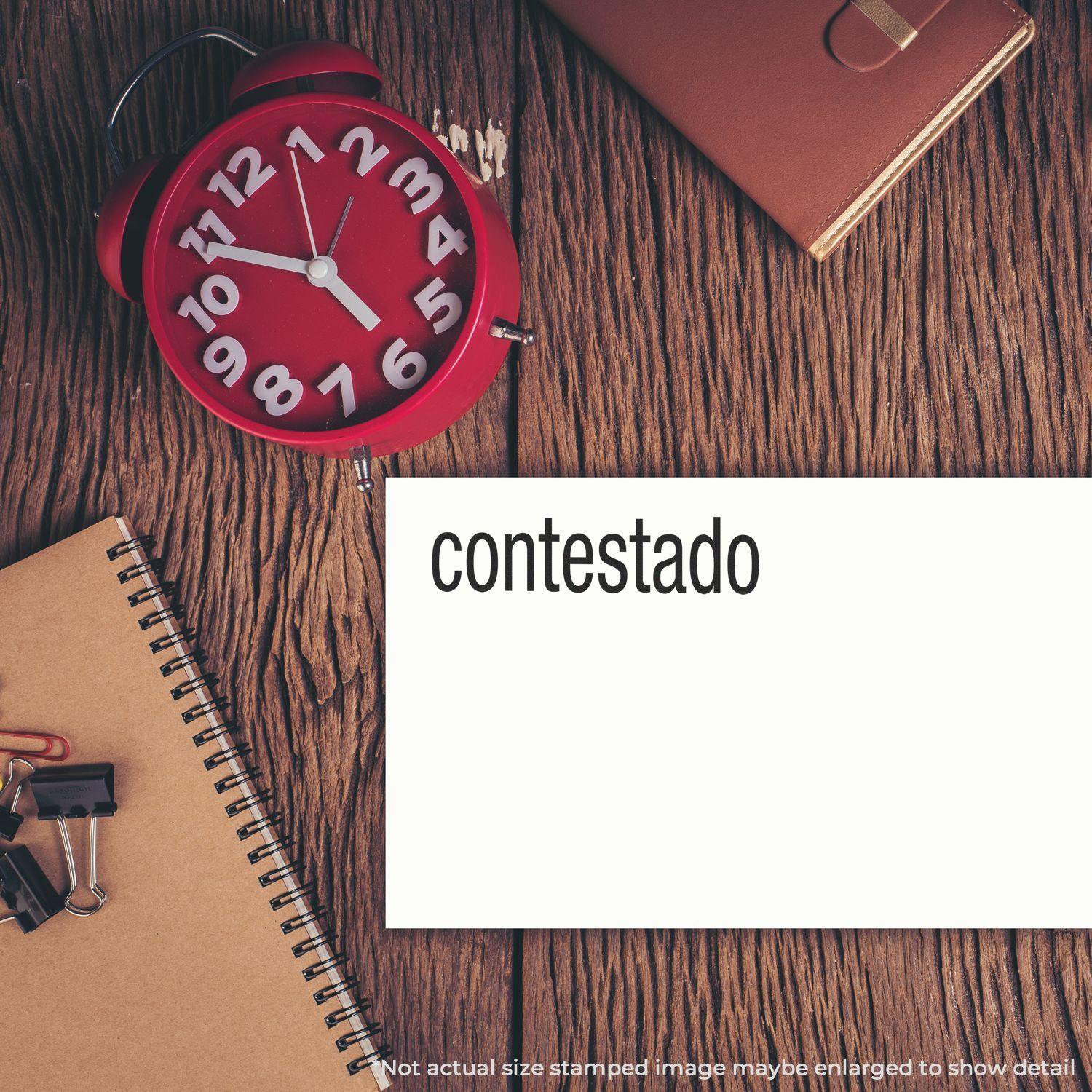 A Contestado Rubber Stamp imprint on white paper, placed on a wooden desk with a red clock, notebook, and office supplies.