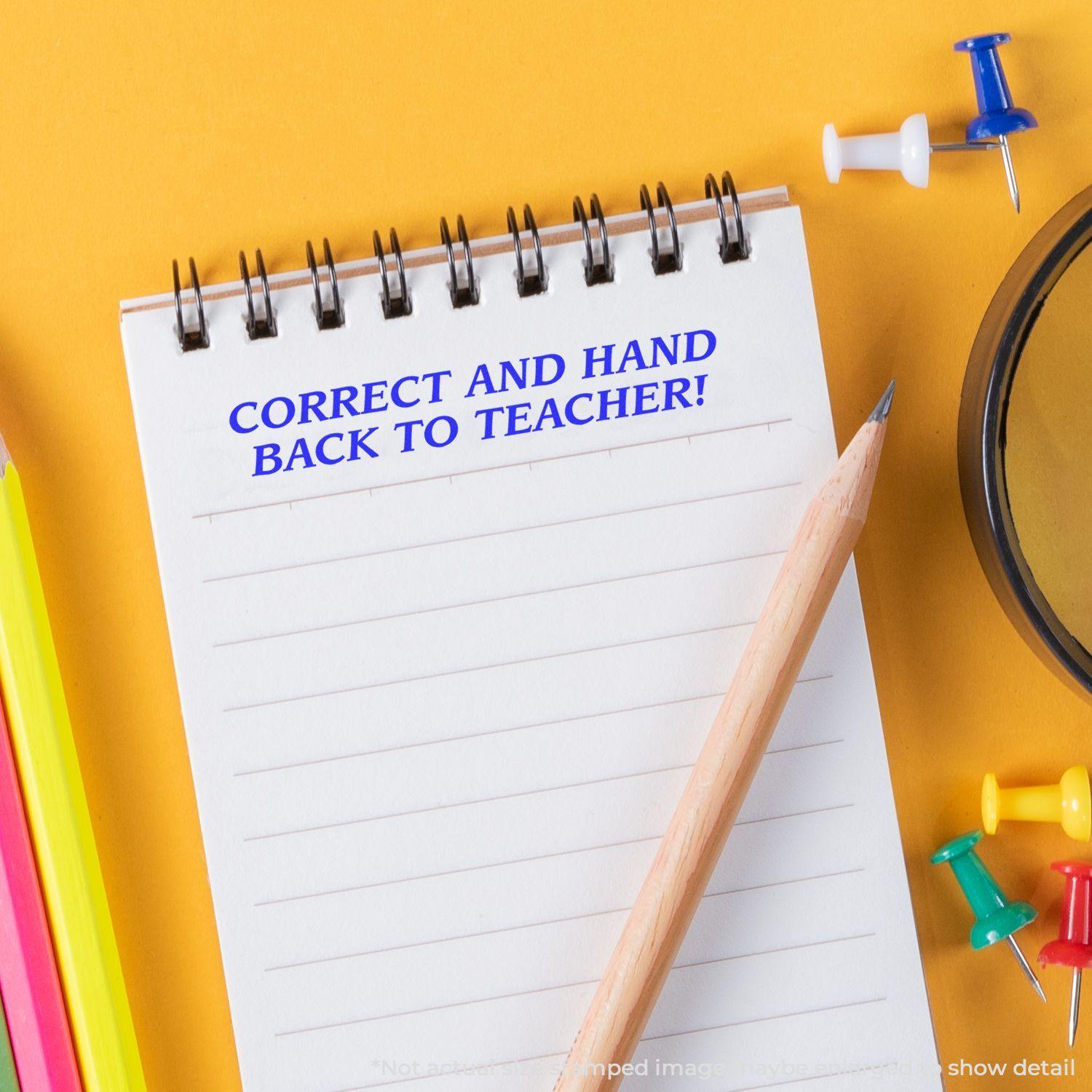 A notebook with CORRECT AND HAND BACK TO TEACHER! stamped in blue ink using the Large Correct And Hand Back To Teacher Rubber Stamp, surrounded by stationery.