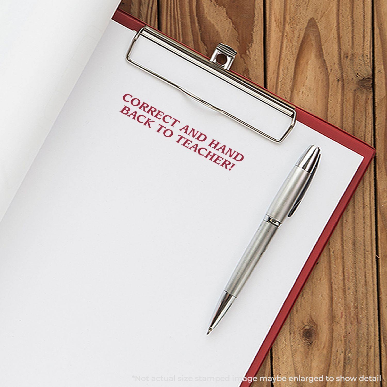 A clipboard with a paper stamped Correct And Hand Back To Teacher using the Large Correct And Hand Back To Teacher Rubber Stamp, next to a pen.