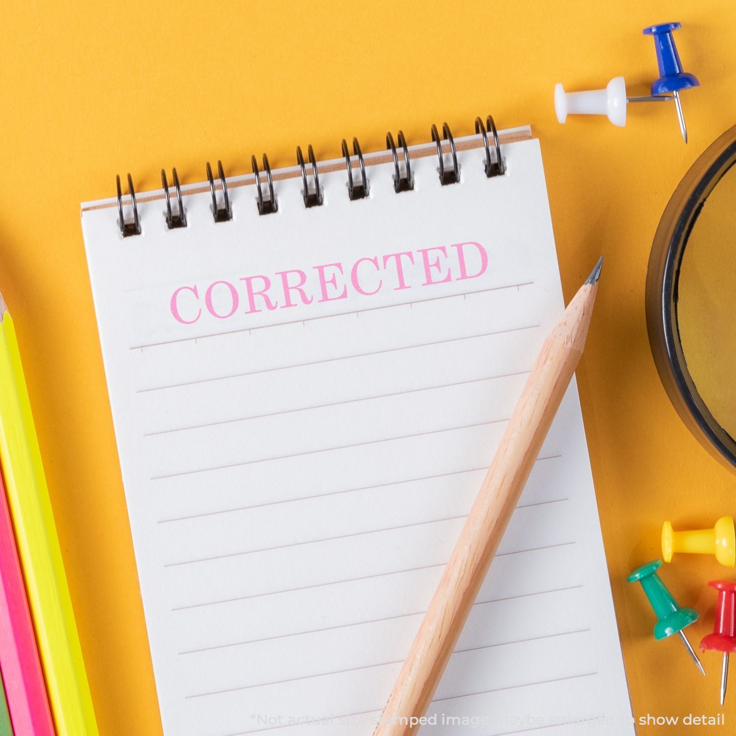 Self Inking Corrected Stamp used on a spiral notebook with a pencil, colorful push pins, and a yellow background.