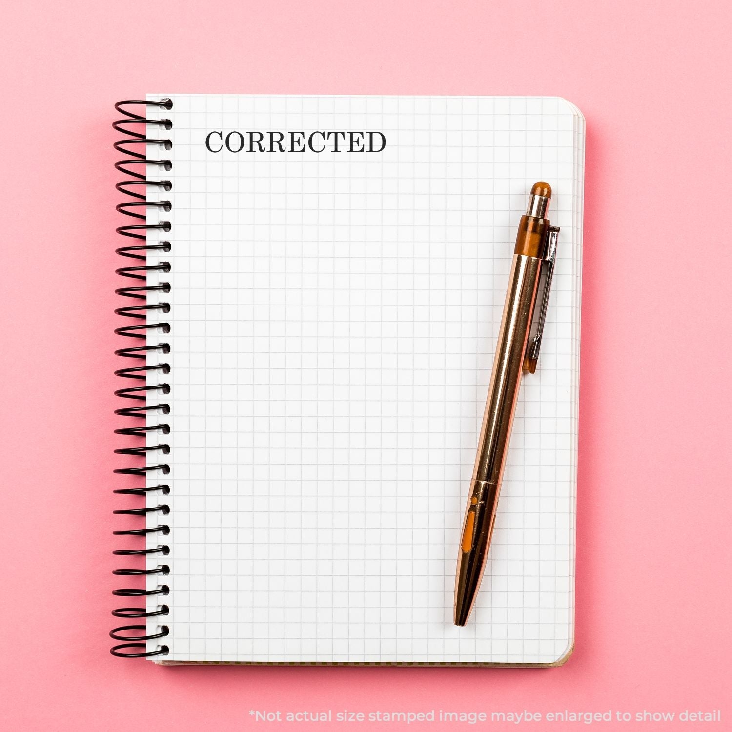 Self Inking Corrected Stamp used on a spiral notebook with a pen placed on a pink background.
