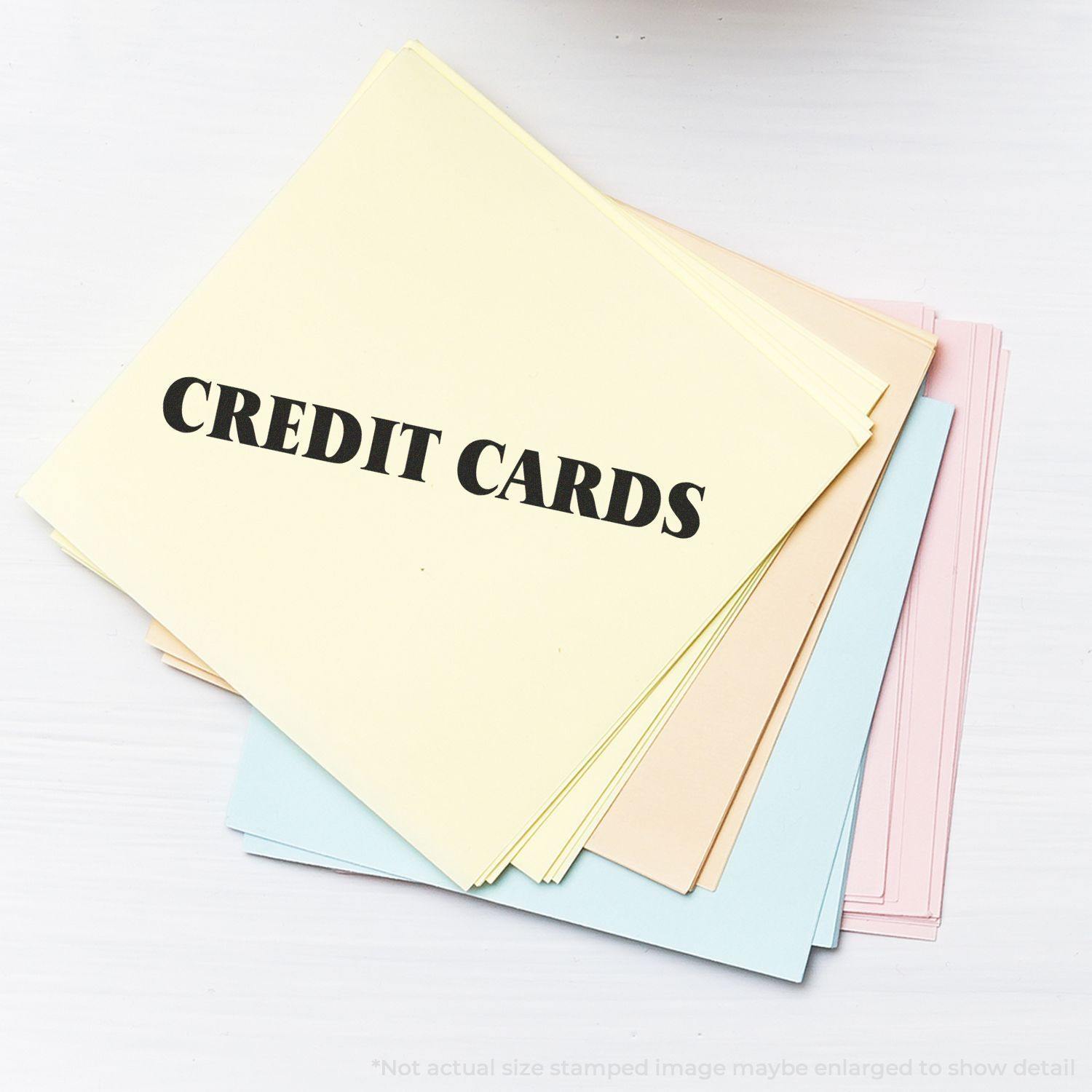 A stack of pastel-colored papers stamped with CREDIT CARDS using the Large Credit Cards Rubber Stamp.