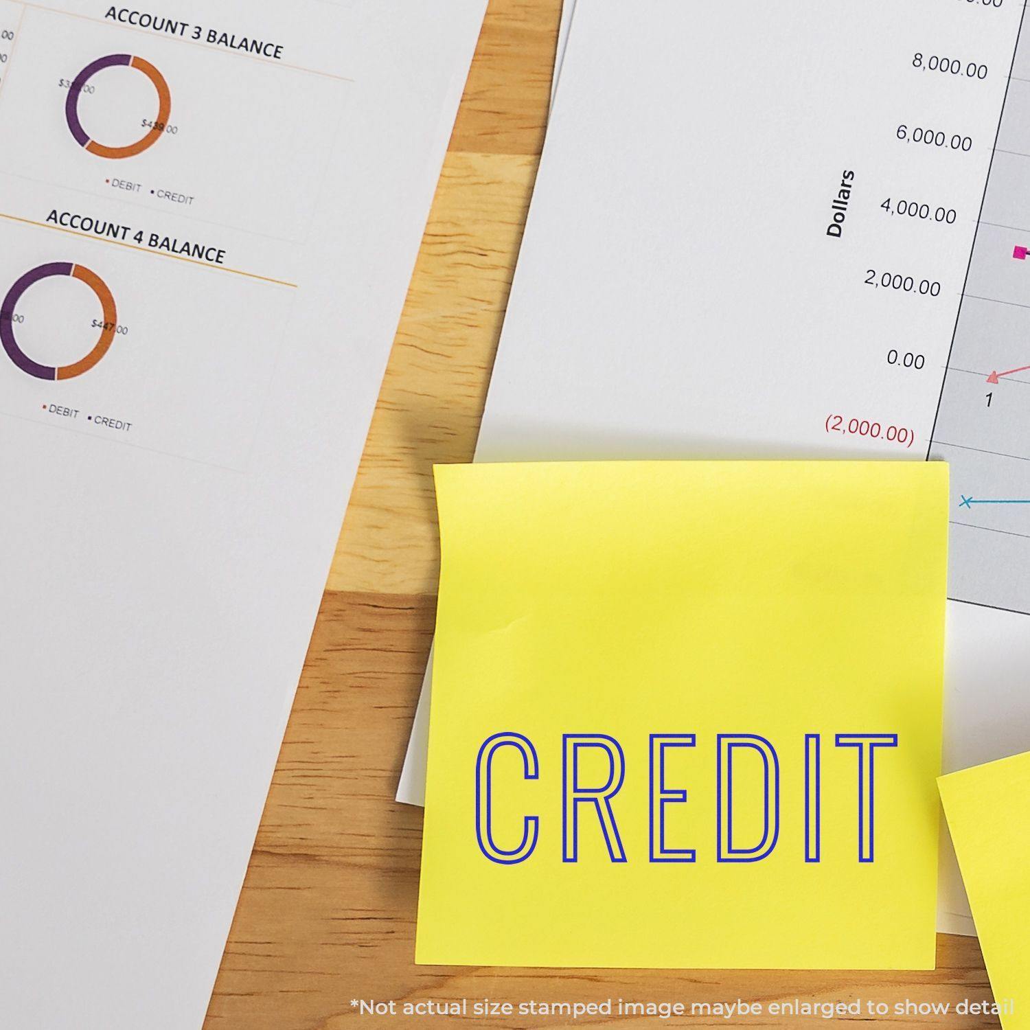 A Large Self Inking Credit Outline Stamp is used on a yellow sticky note labeled CREDIT next to financial documents on a wooden desk.