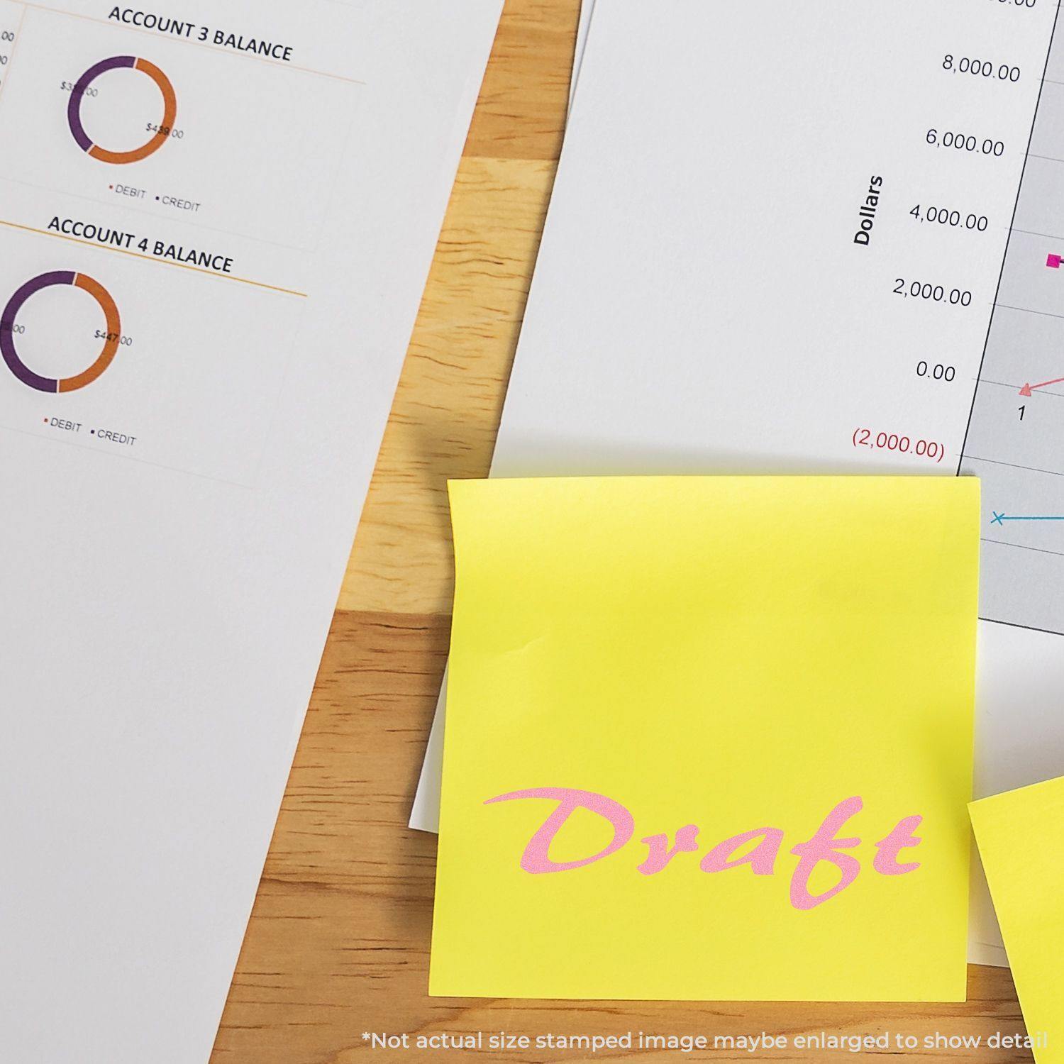 Self Inking Cursive Draft Stamp used on a yellow sticky note, placed on a wooden desk next to financial documents and charts.