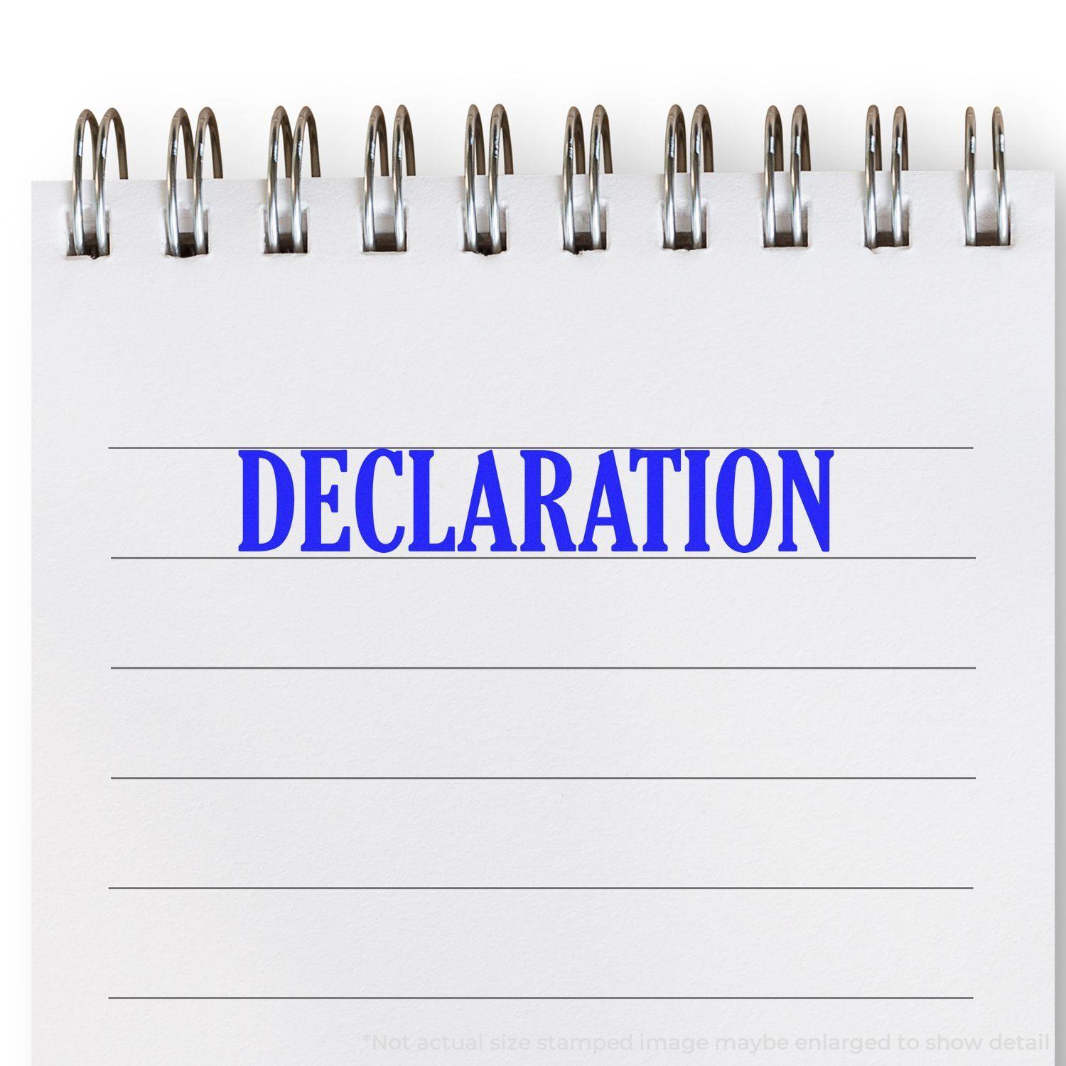 Slim Pre-Inked Declaration Stamp used on a spiral notebook, showing the word DECLARATION in bold blue letters on lined paper.