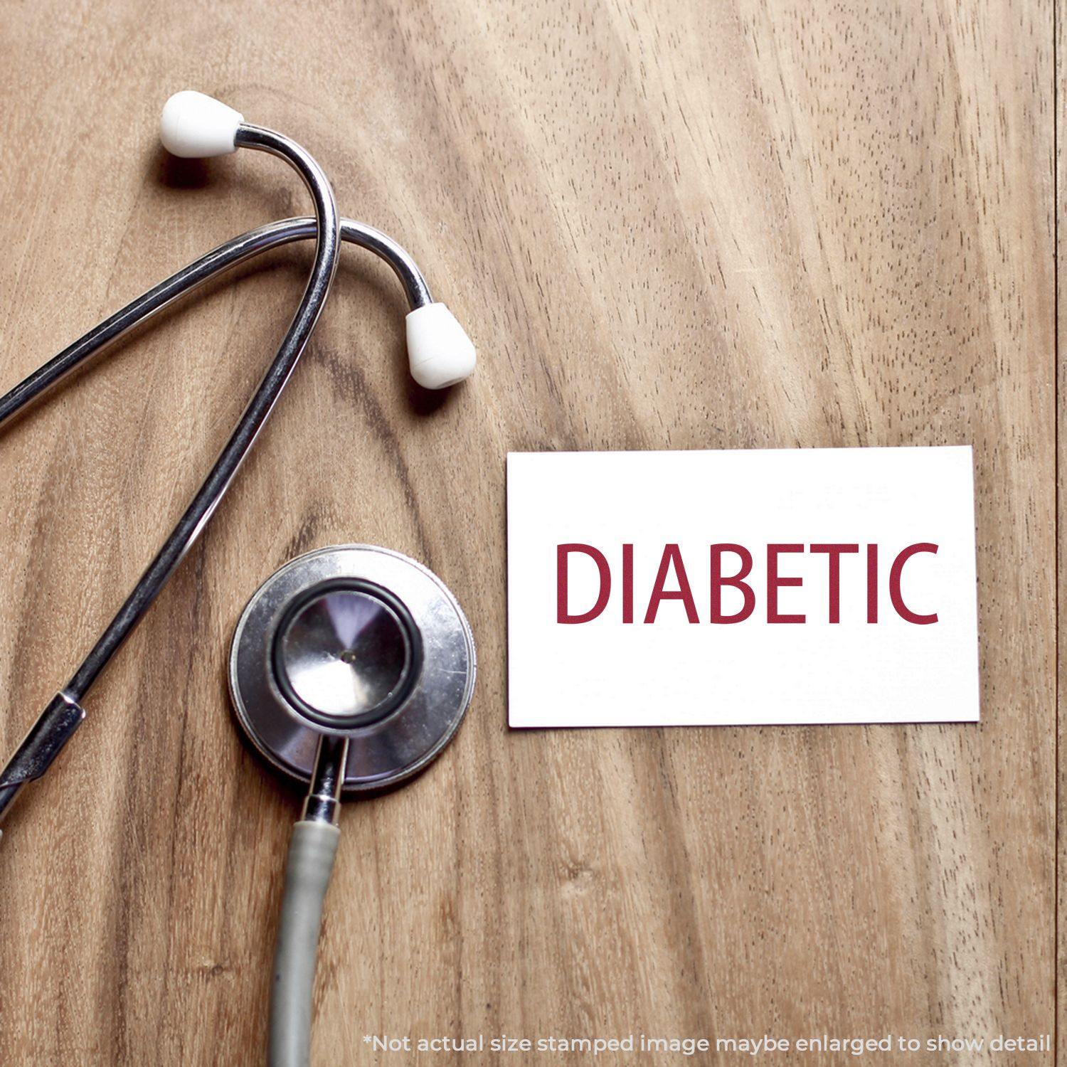 Large Self Inking Diabetic Stamp imprint on a white card next to a stethoscope on a wooden surface.