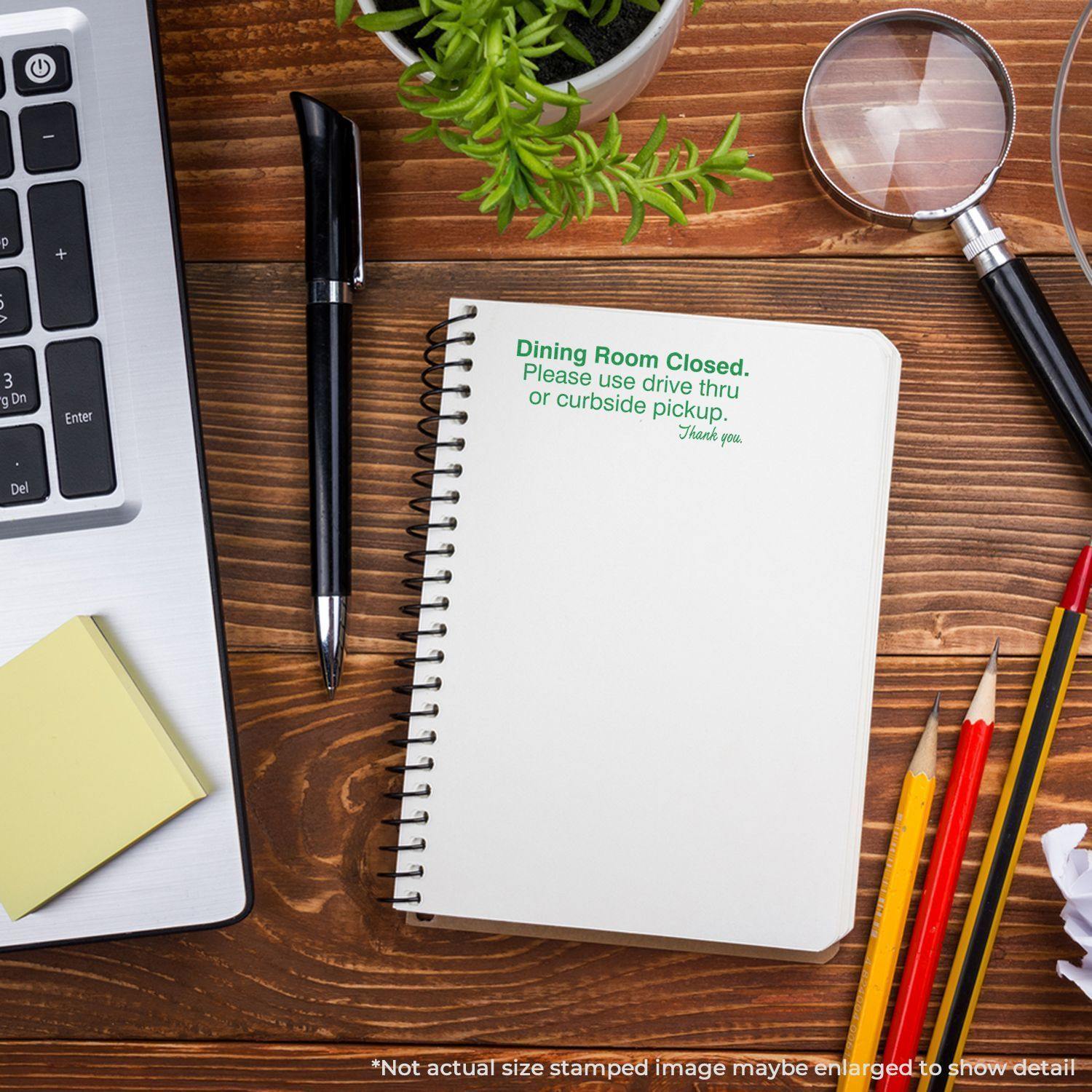 Large Self Inking Dining Room Closed Stamp used on a notebook, placed on a wooden desk with a laptop, plant, pens, and magnifying glass.