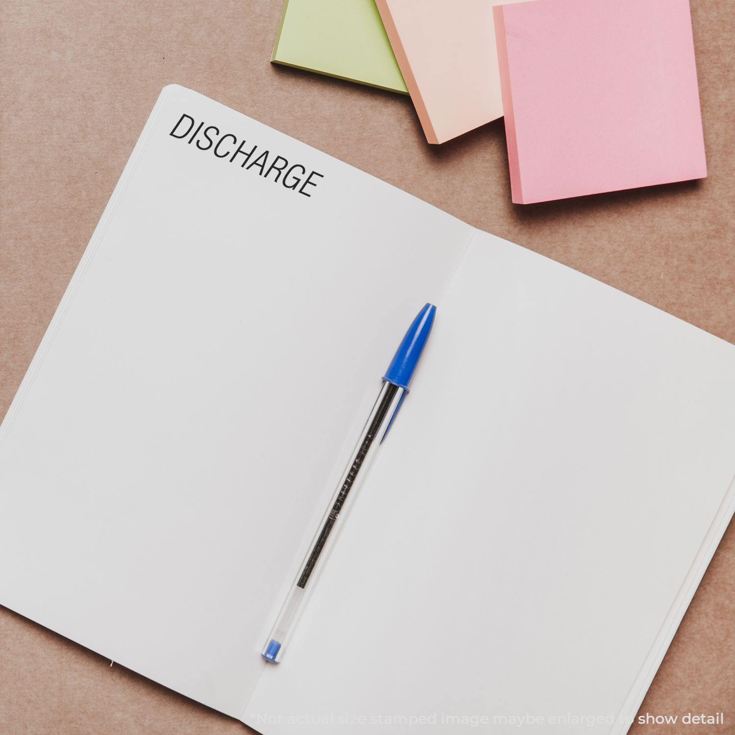 Slim Pre-Inked Discharge Stamp used on an open notebook with a blue pen and colorful sticky notes in the background.