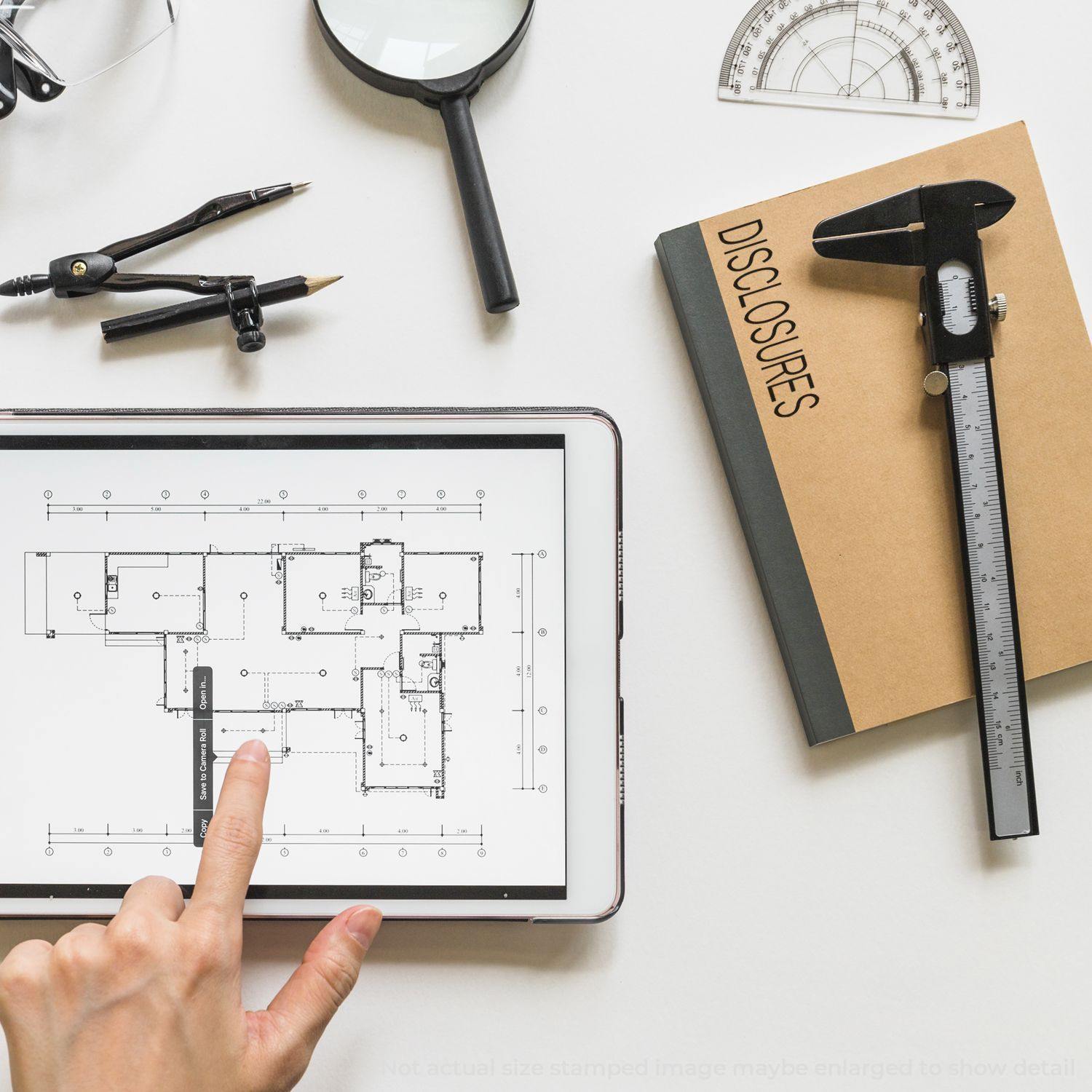 A workspace with a Self Inking Disclosures Stamp, a tablet displaying a floor plan, a compass, a magnifying glass, and a caliper.