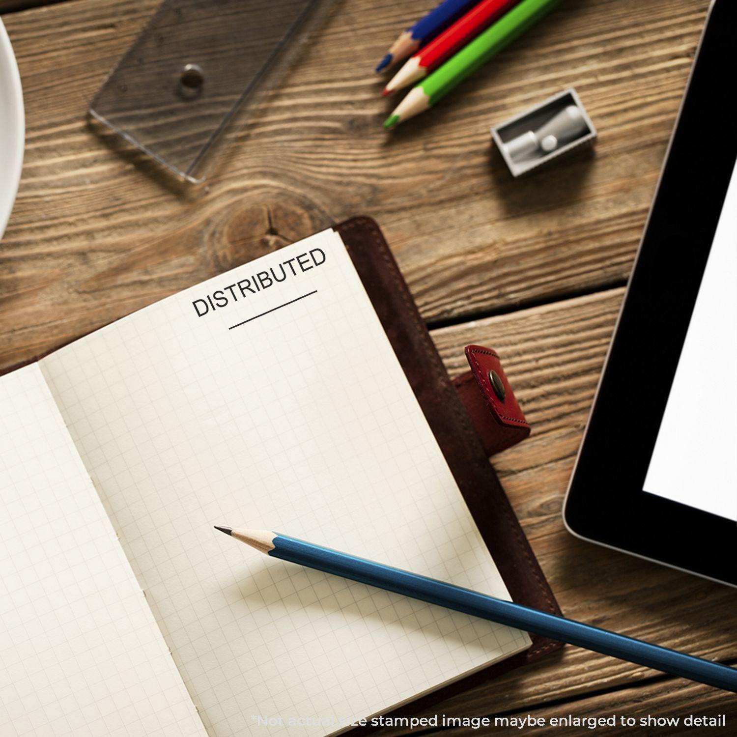 Slim Pre-Inked Distributed Stamp With Line used on a notebook page, surrounded by pencils, a sharpener, and a tablet on a wooden desk.