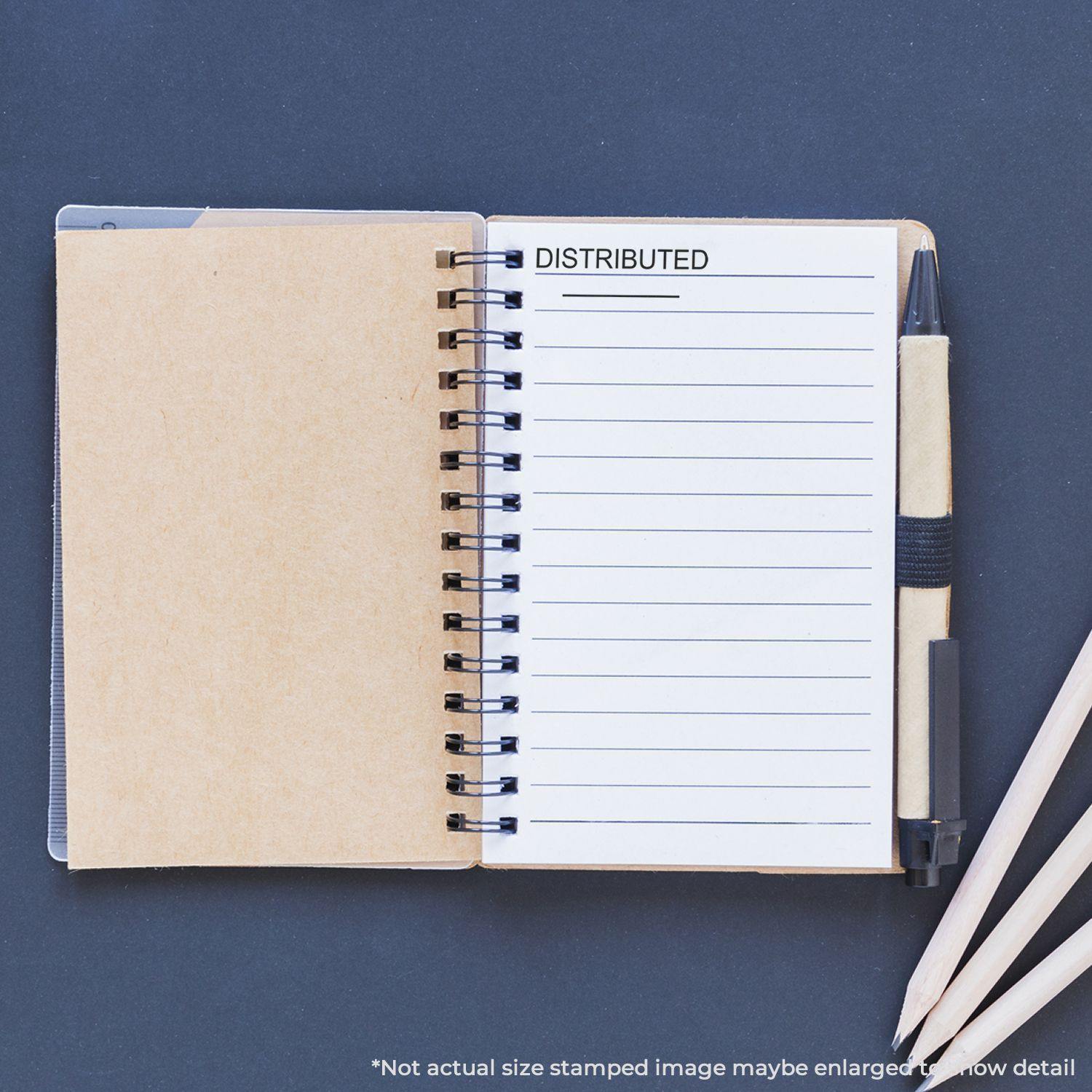 Large Self Inking Distributed Stamp With Line used on a notebook page, with a pen and pencils placed beside the notebook.