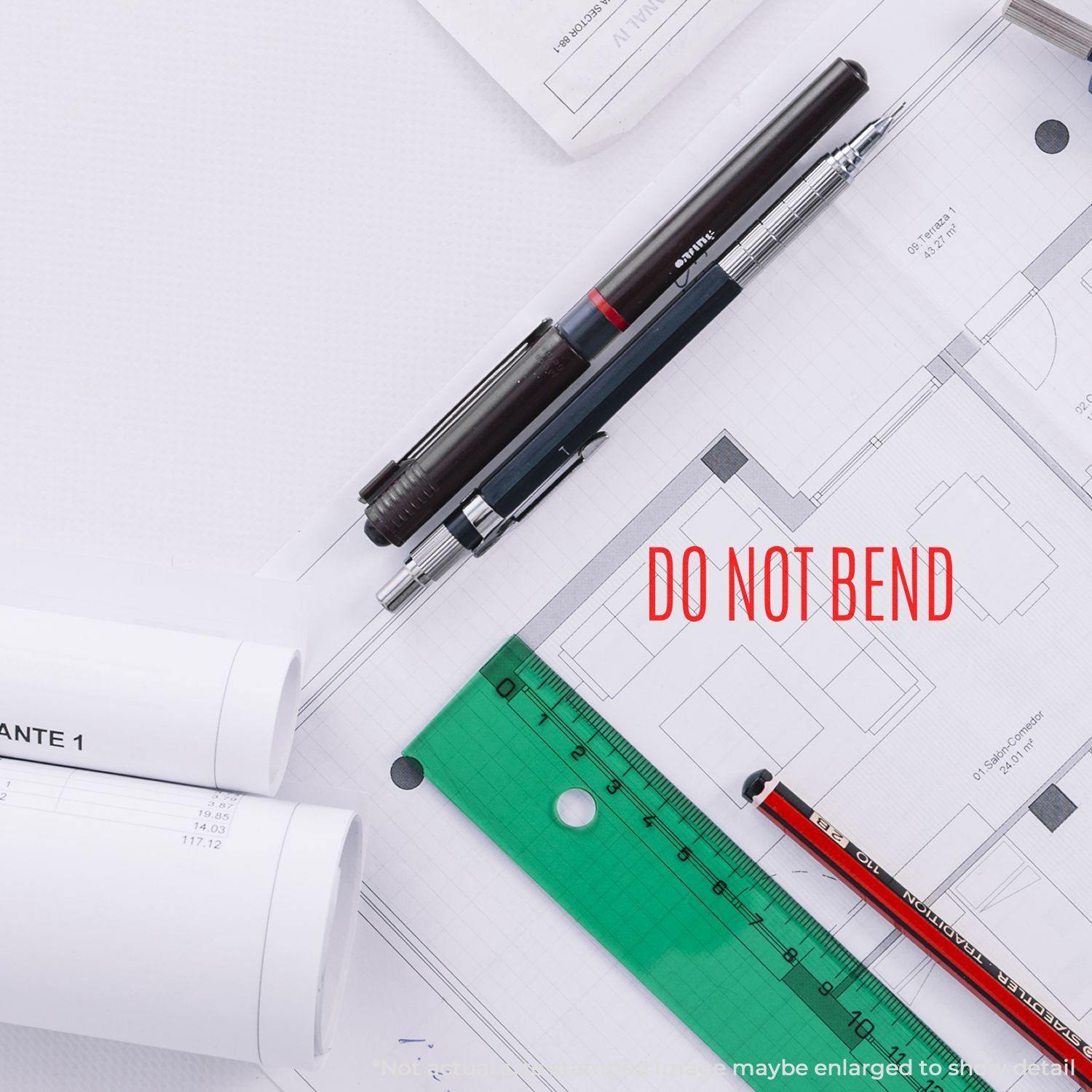 Self Inking Do Not Bend Stamp used on architectural plans, surrounded by pens, a ruler, and rolled-up documents.