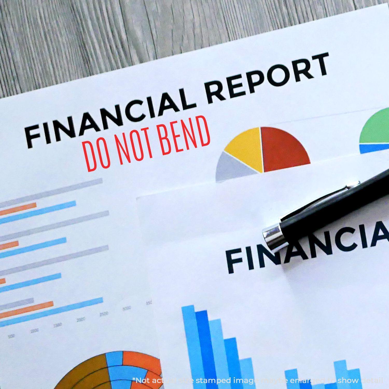 Financial report stamped with Large Self Inking Do Not Bend Stamp in red ink, placed on a wooden surface with a pen on top.