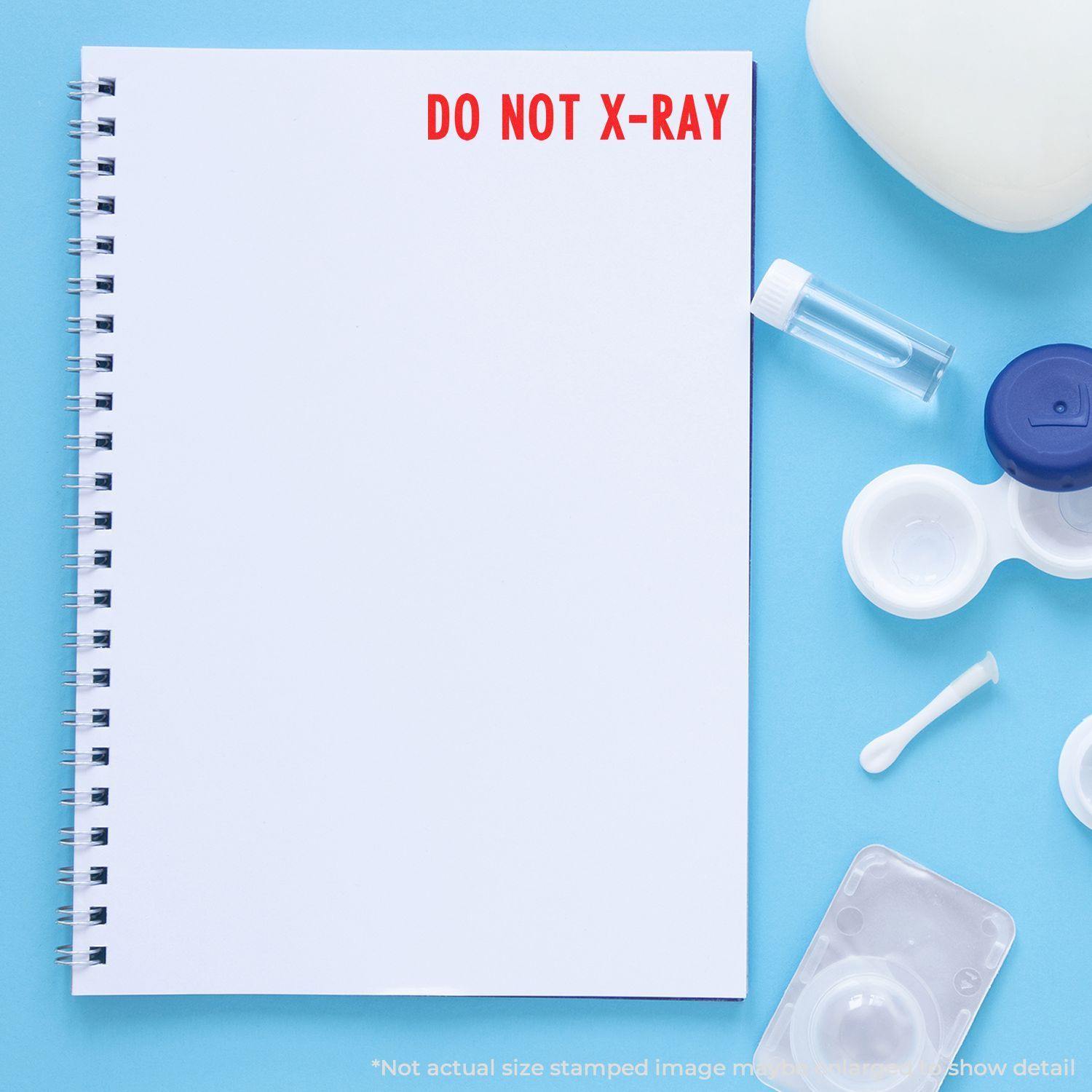 Slim Pre-Inked Do Not X-Ray Stamp used on a blank notebook page, surrounded by medical items on a blue background.