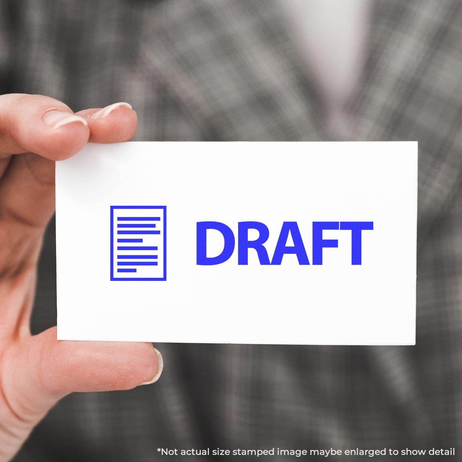 A hand holding a white card stamped with DRAFT in blue using the Self Inking Draft with Letter Stamp. Background shows a blurred plaid pattern.