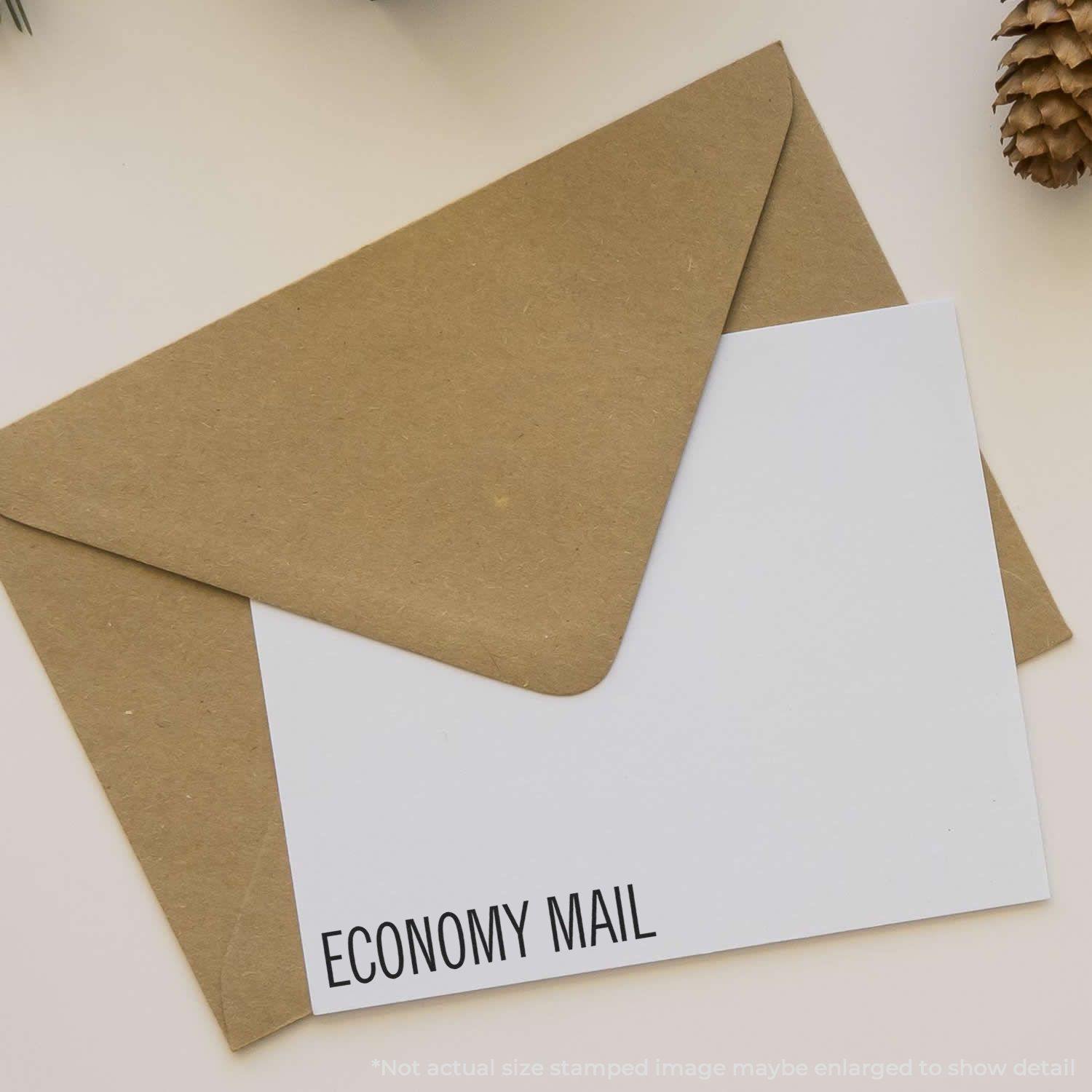 A brown envelope with a white card stamped ECONOMY MAIL using the Self Inking Economy Mail Stamp, placed on a light-colored surface.