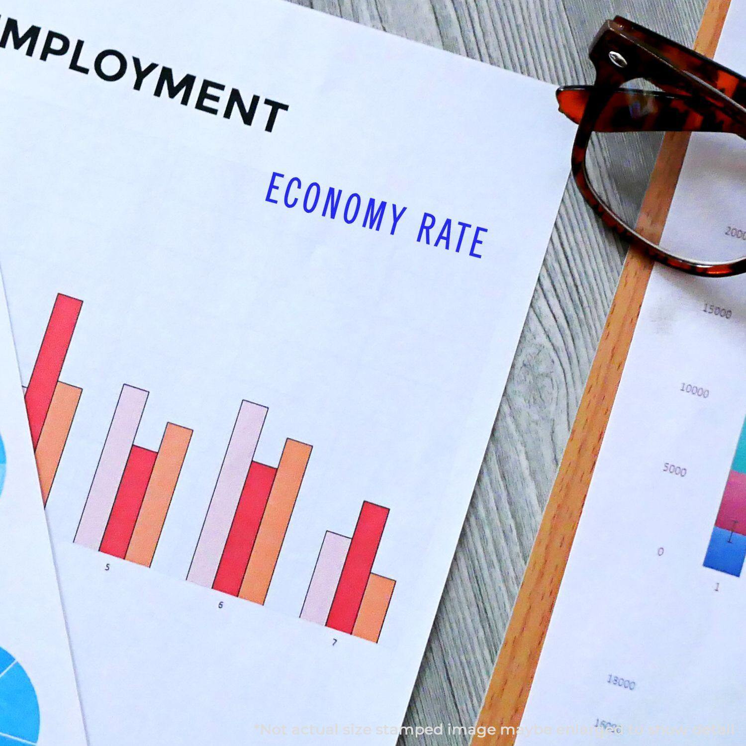 Slim Pre-Inked Economy Rate Stamp used on a document with employment charts and graphs, next to eyeglasses on a desk.