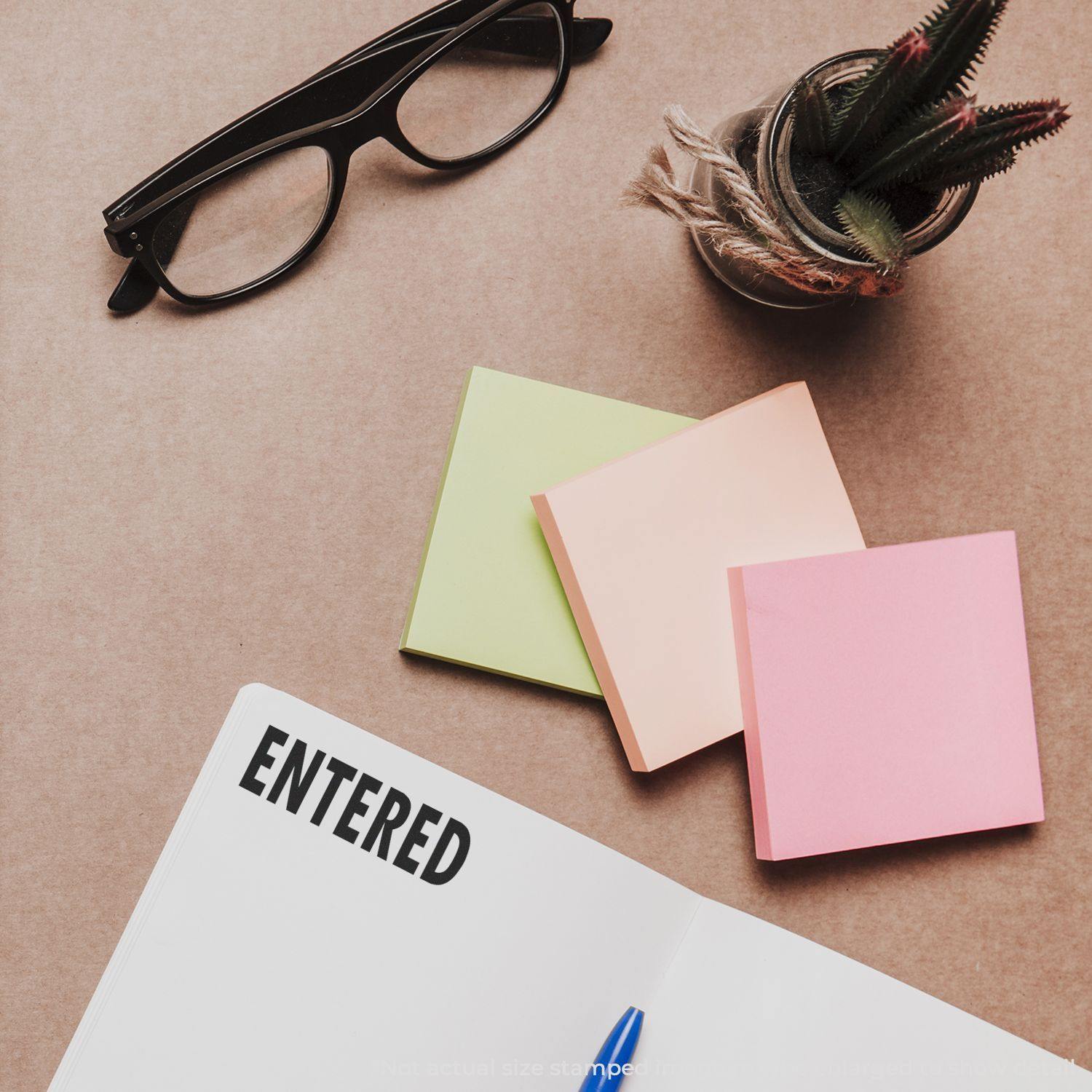 Entered Rubber Stamp on a document, surrounded by glasses, sticky notes, a pen, and a small potted plant on a brown desk.