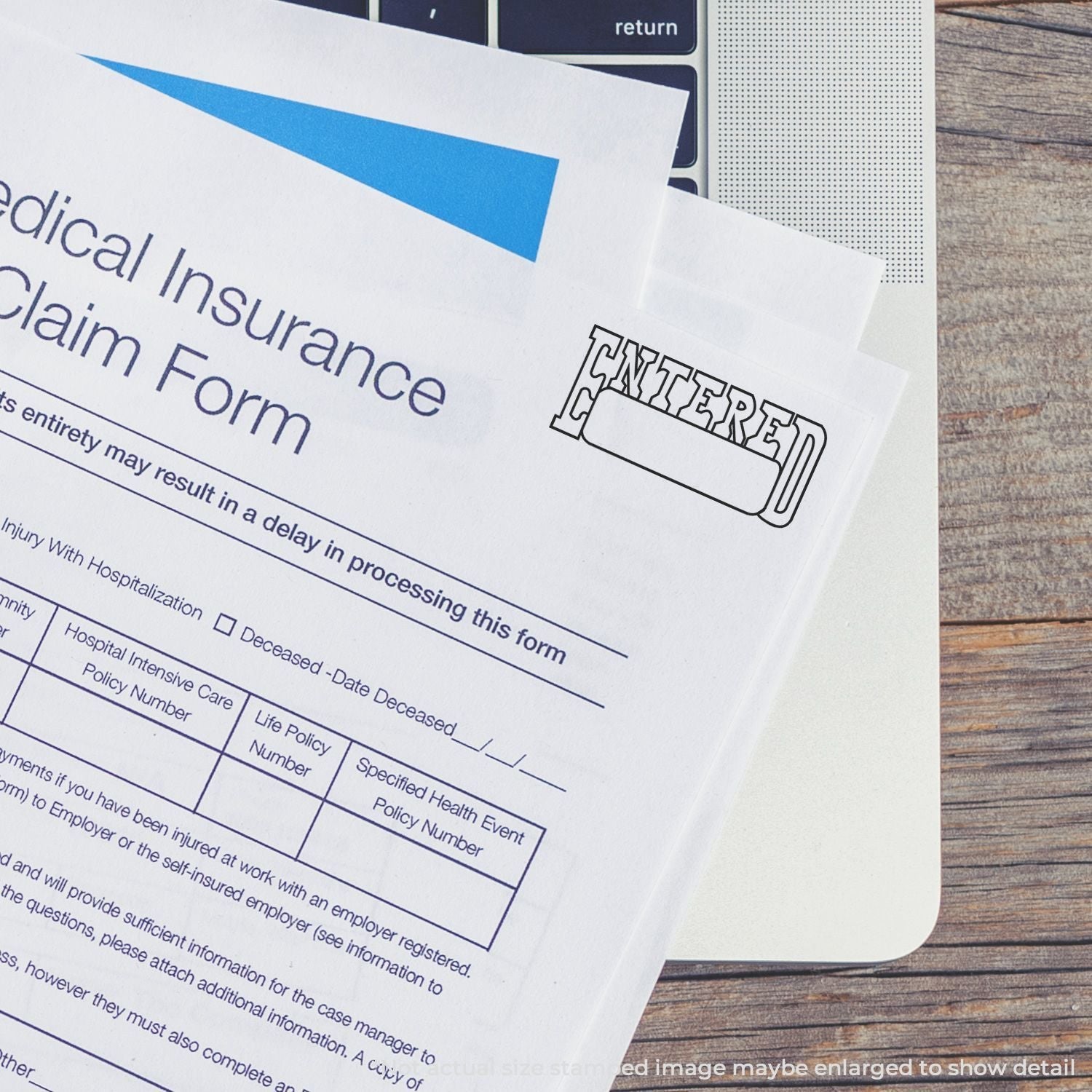 Slim Pre-Inked Entered with Date Box Stamp used on a medical insurance claim form placed on a laptop keyboard.