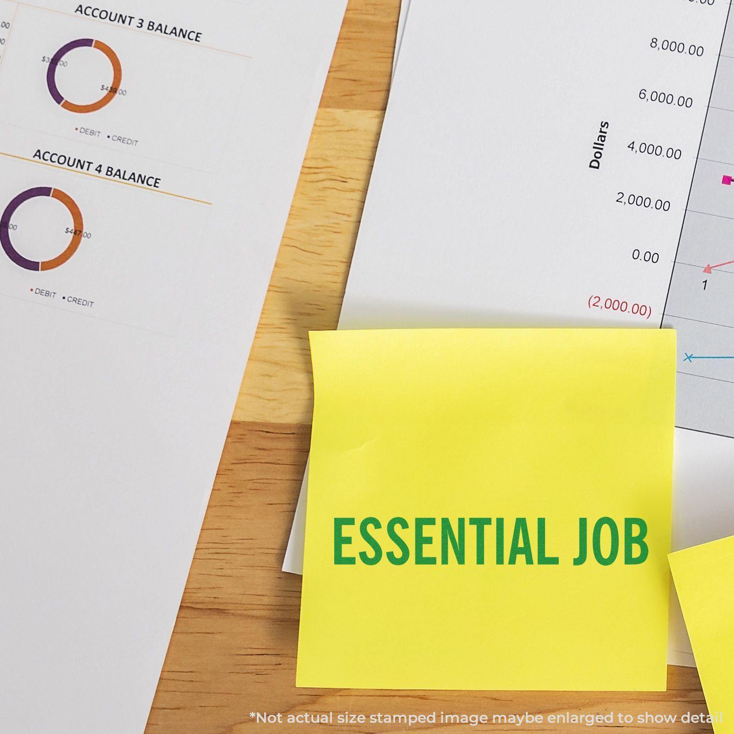 Large Essential Job Rubber Stamp used on a yellow sticky note, placed on a desk with financial documents and charts in the background.