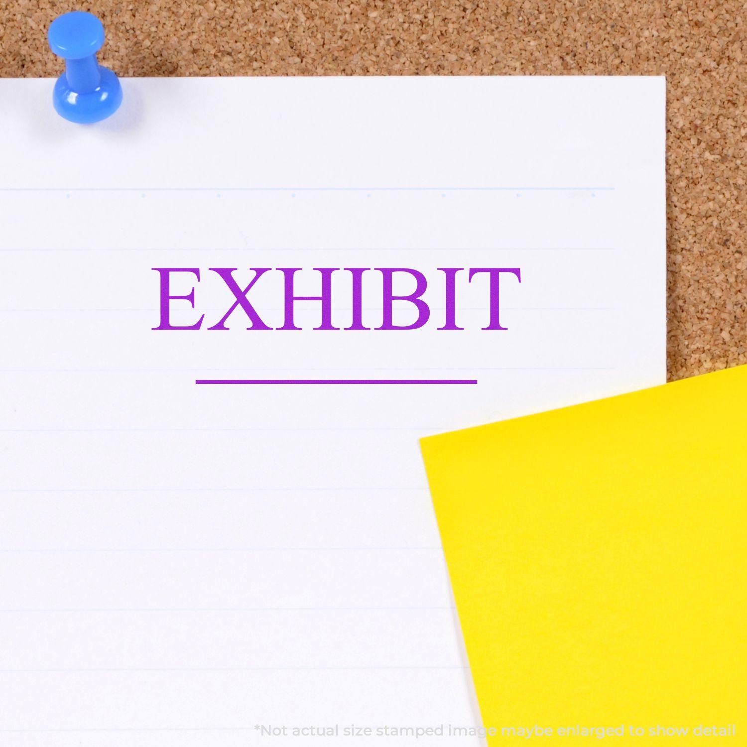 Large Exhibit Rubber Stamp imprint on a white paper pinned to a corkboard, with a yellow sticky note partially visible.