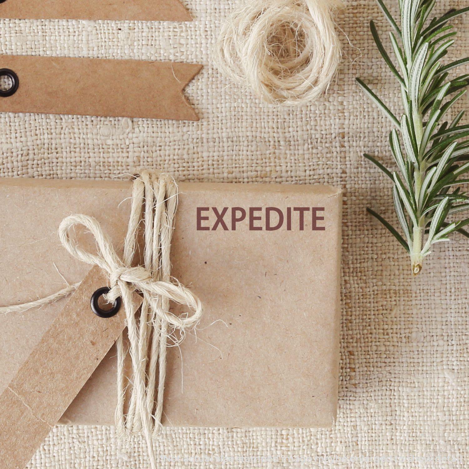 A package wrapped in brown paper and twine is stamped with EXPEDITE using the Large Pre-Inked Expedite Stamp, surrounded by rustic decor.