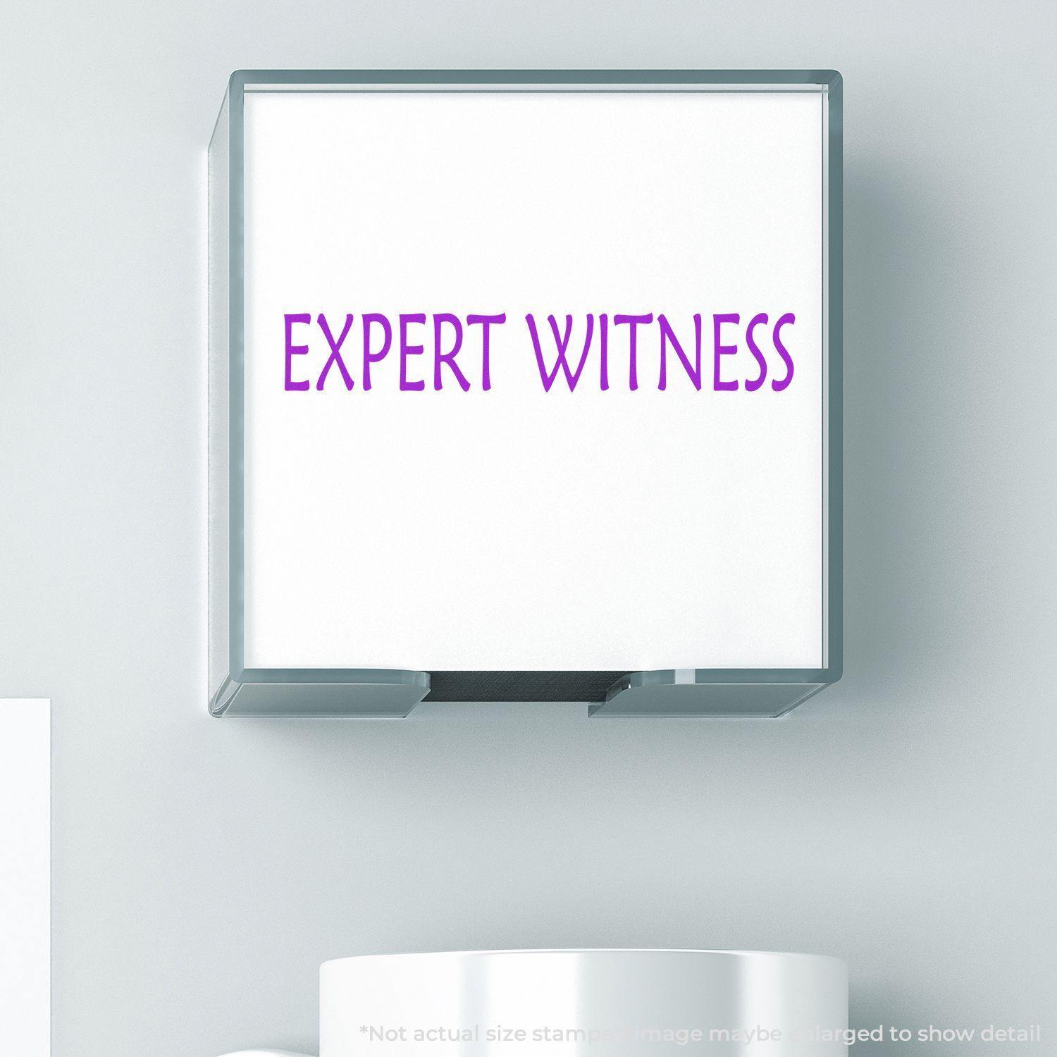 Expert Witness Rubber Stamp in use, showing the text EXPERT WITNESS in purple on a white background, with a cup partially visible below.