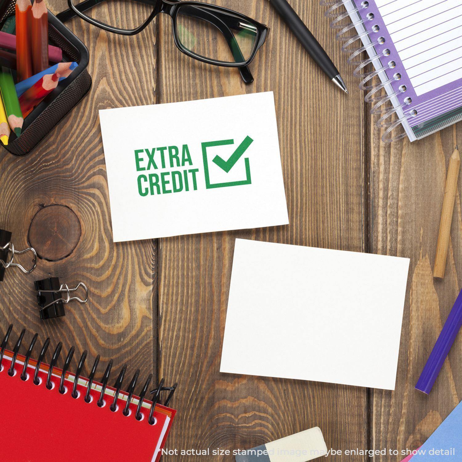 Self Inking Extra Credit Stamp on a wooden desk with stationery items, including notebooks, glasses, and colorful pens.