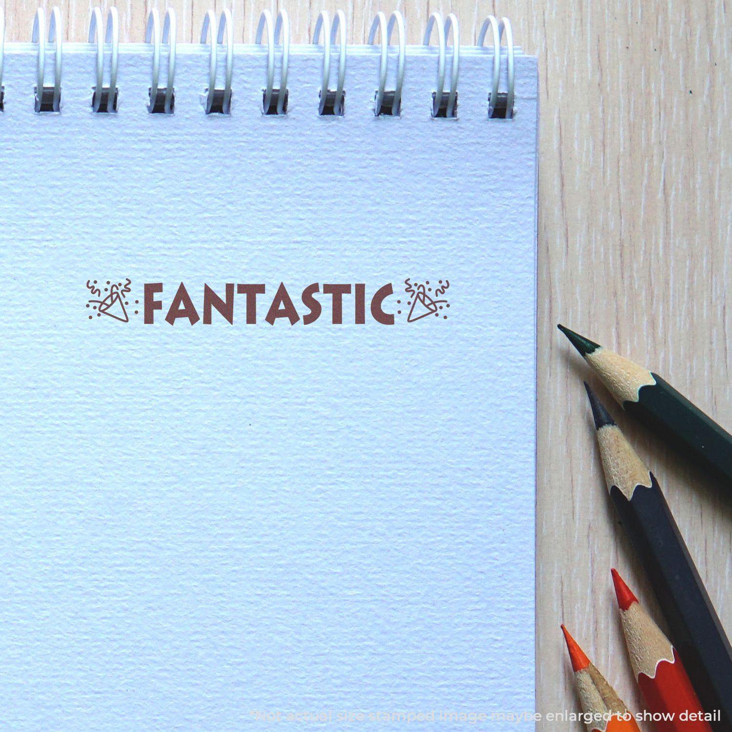 A notebook with the Self Inking Fantastic with Icons Stamp imprint on a page, surrounded by colored pencils on a wooden surface.