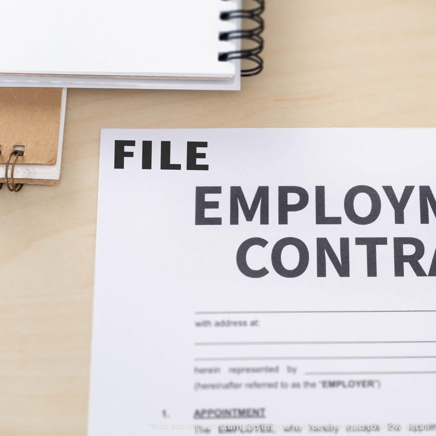 Slim Pre-Inked File Stamp marking FILE on an employment contract, with notebooks in the background on a wooden desk.