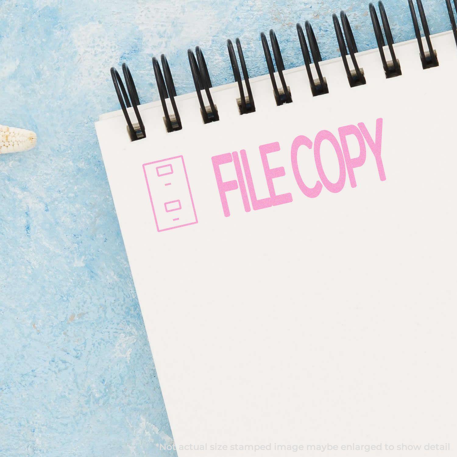 Self Inking File Copy with Drawer Stamp in pink ink on a white spiral notebook, placed on a light blue textured surface.