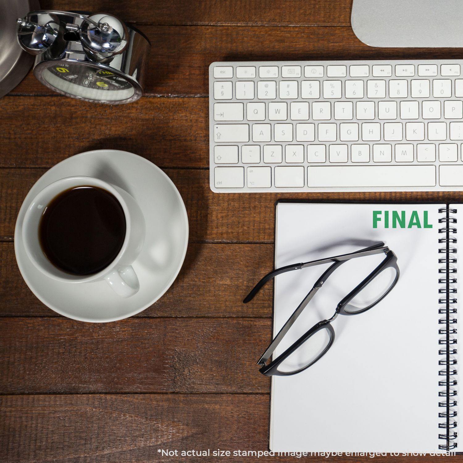 Large Self Inking Final Stamp on a notepad next to glasses, a keyboard, a coffee cup, and an alarm clock on a wooden desk.