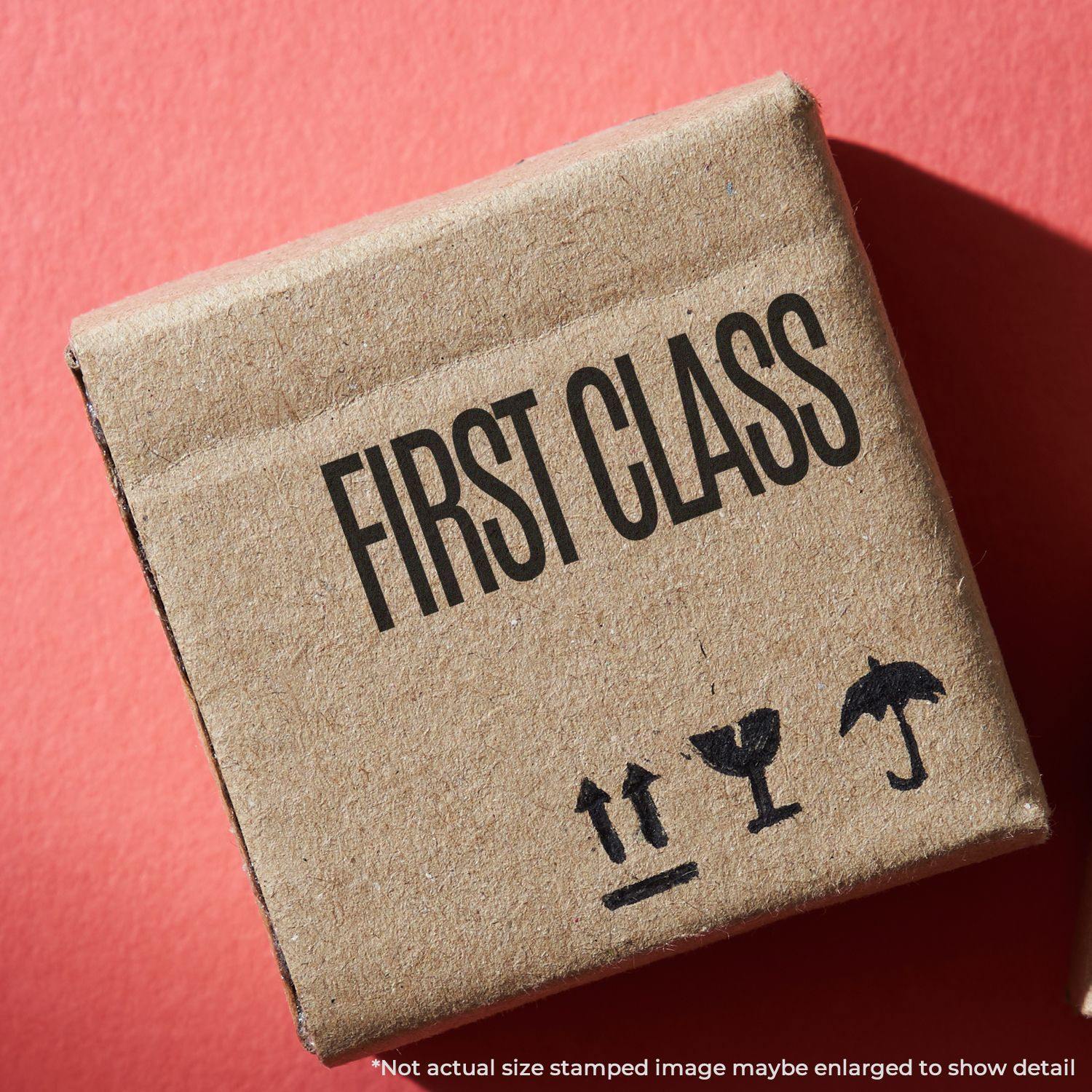 A cardboard box stamped with FIRST CLASS using a Self Inking First Class Stamp, placed on a red surface.