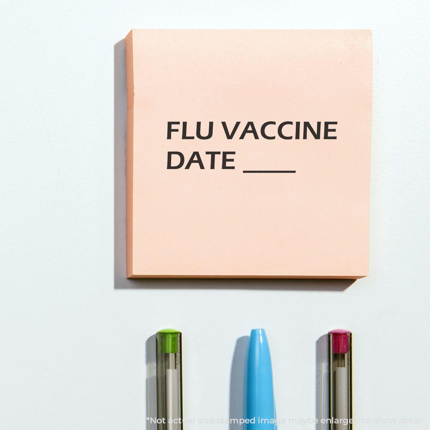 Self Inking Flu Vaccine Date Stamp used on a pink sticky note with FLU VACCINE DATE text, and three pens below the note.