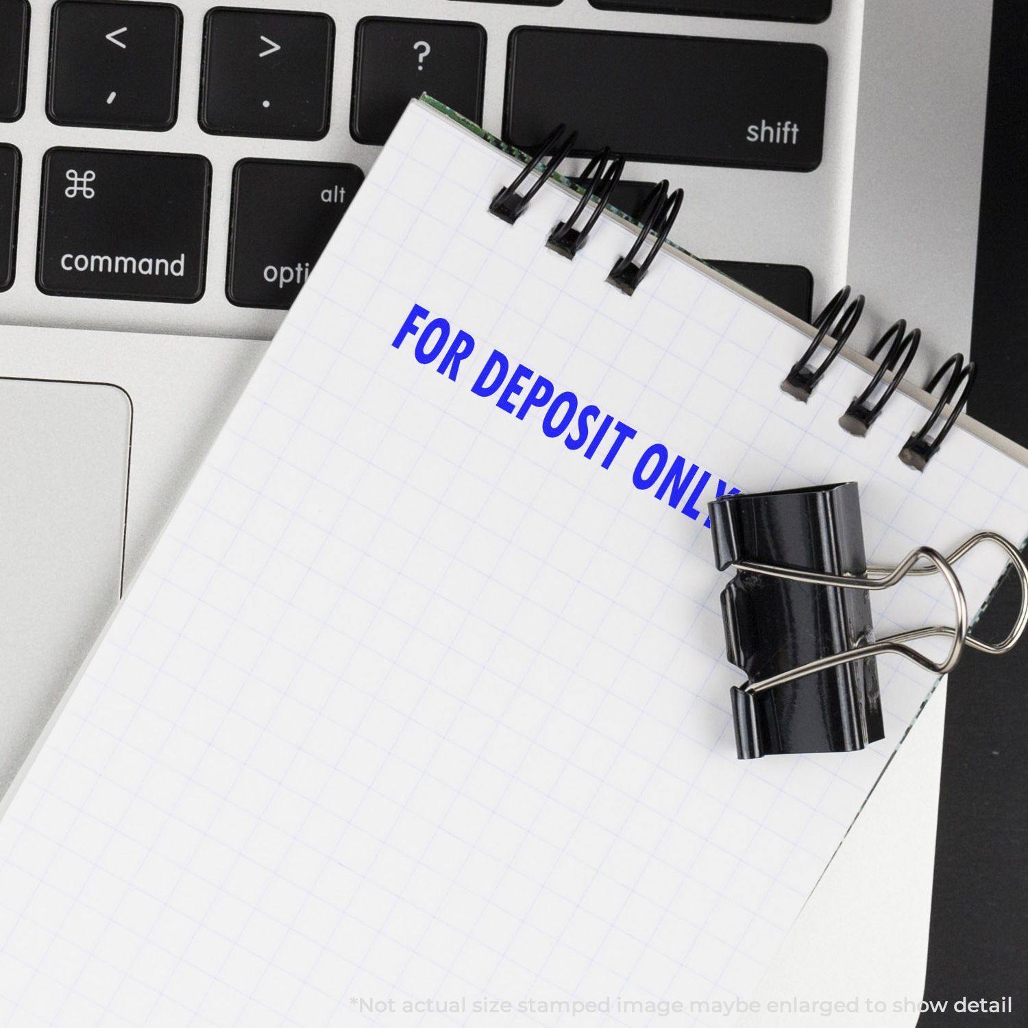 A Large Pre-Inked For Deposit Only Stamp imprint on a notepad, placed on a laptop keyboard with a black binder clip attached.