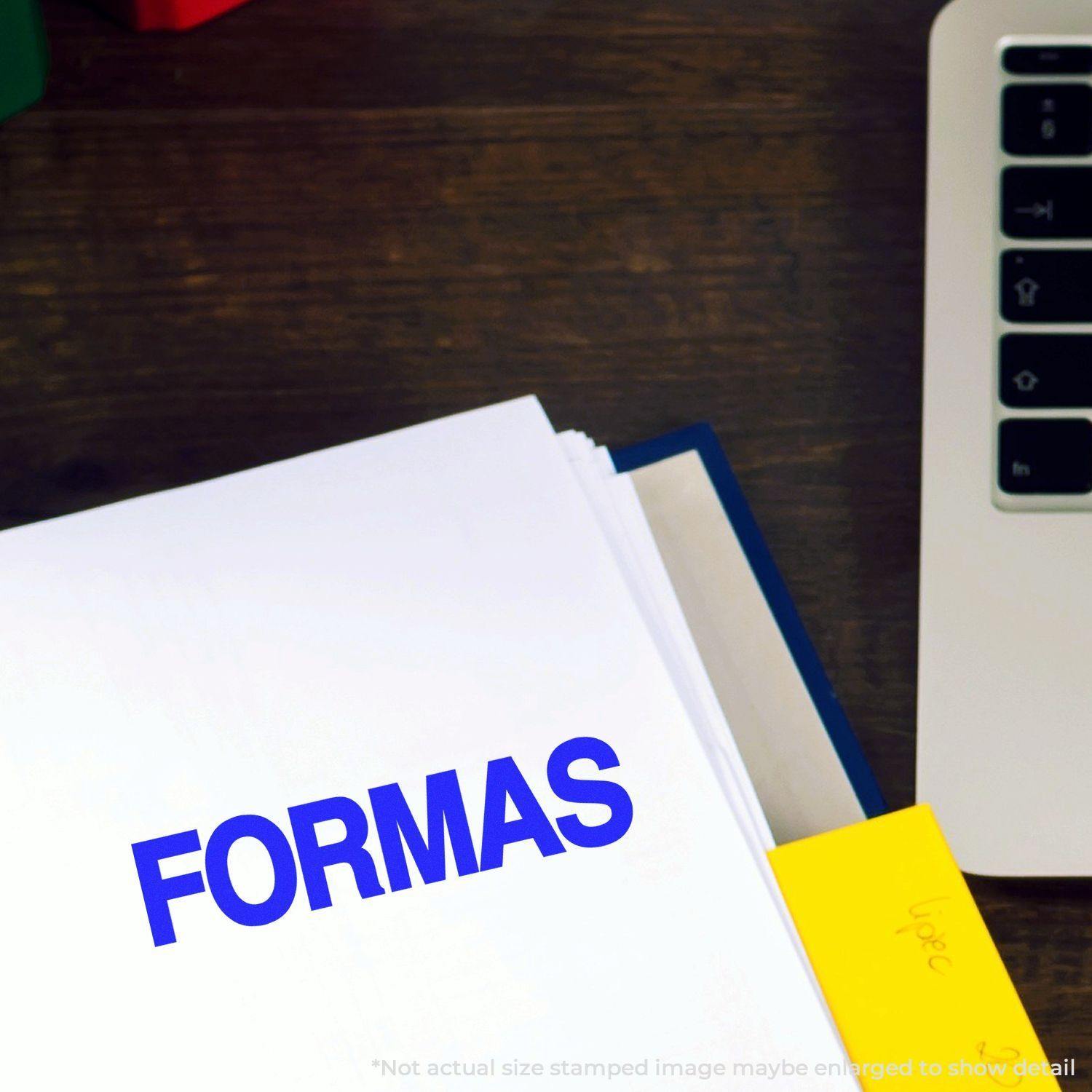 Large Self Inking Formas Stamp imprinting FORMAS in blue on a white document, placed on a wooden desk next to a laptop.