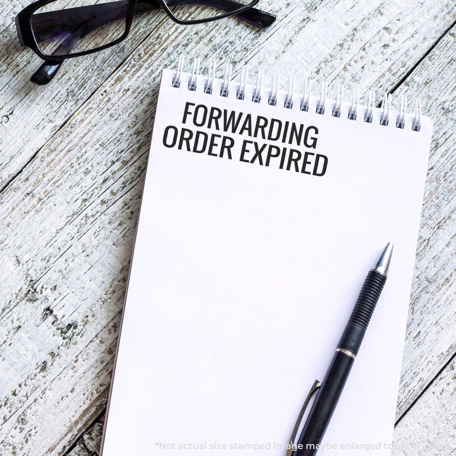 Self Inking Forwarding Order Expiring Stamp used on a notepad with FORWARDING ORDER EXPIRED text, next to a pen and glasses on a wooden surface.
