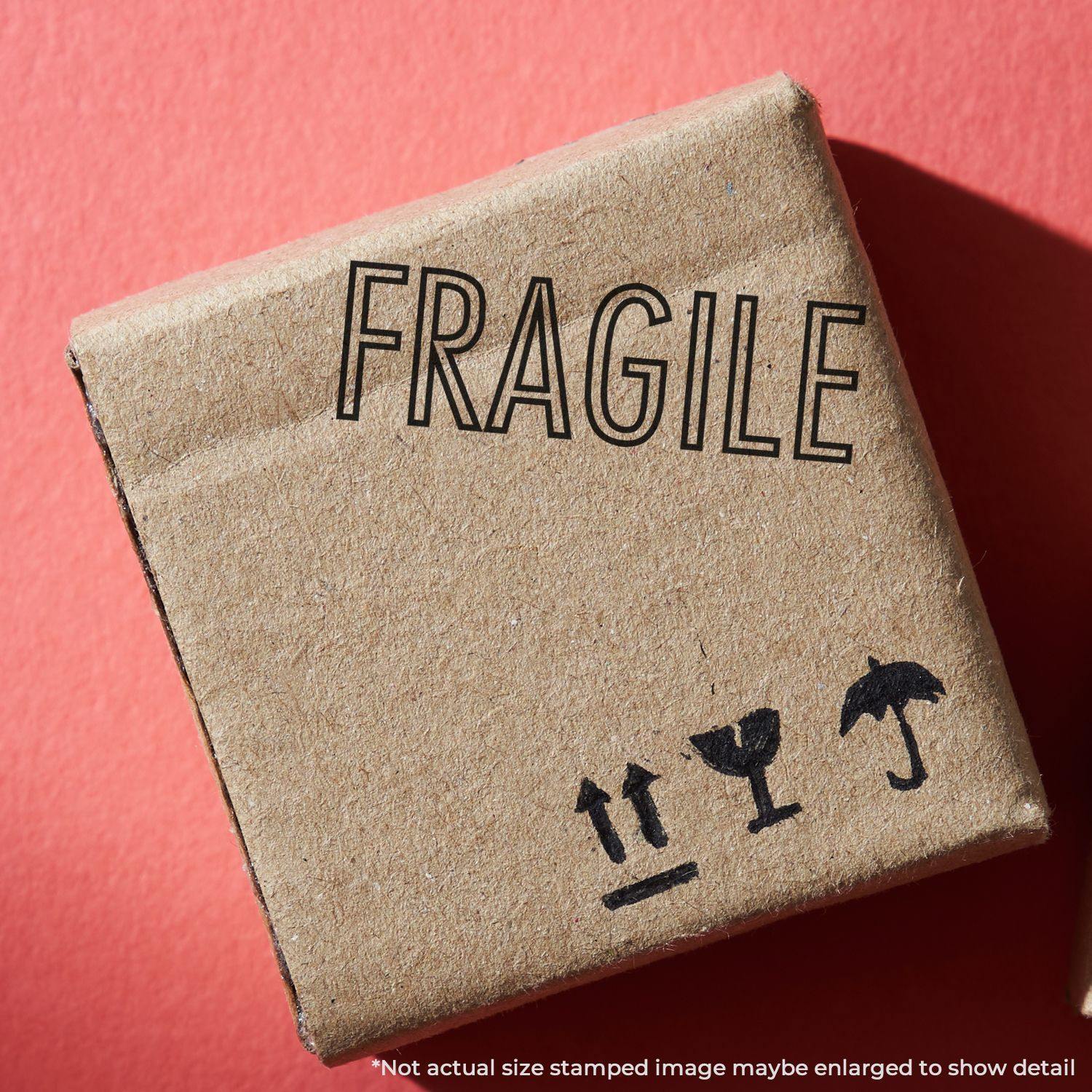 A cardboard box stamped with a Slim Pre-Inked Fragile Stamp, showing FRAGILE and handling symbols on a red background.